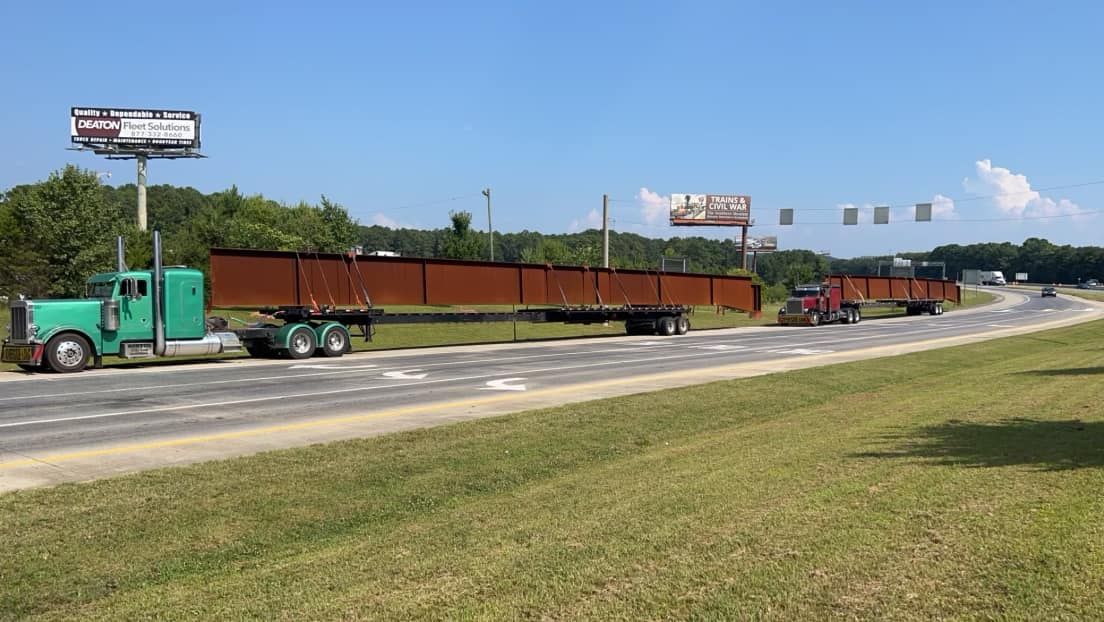 A semi truck is driving down a highway with a large yellow bucket on the back of it.