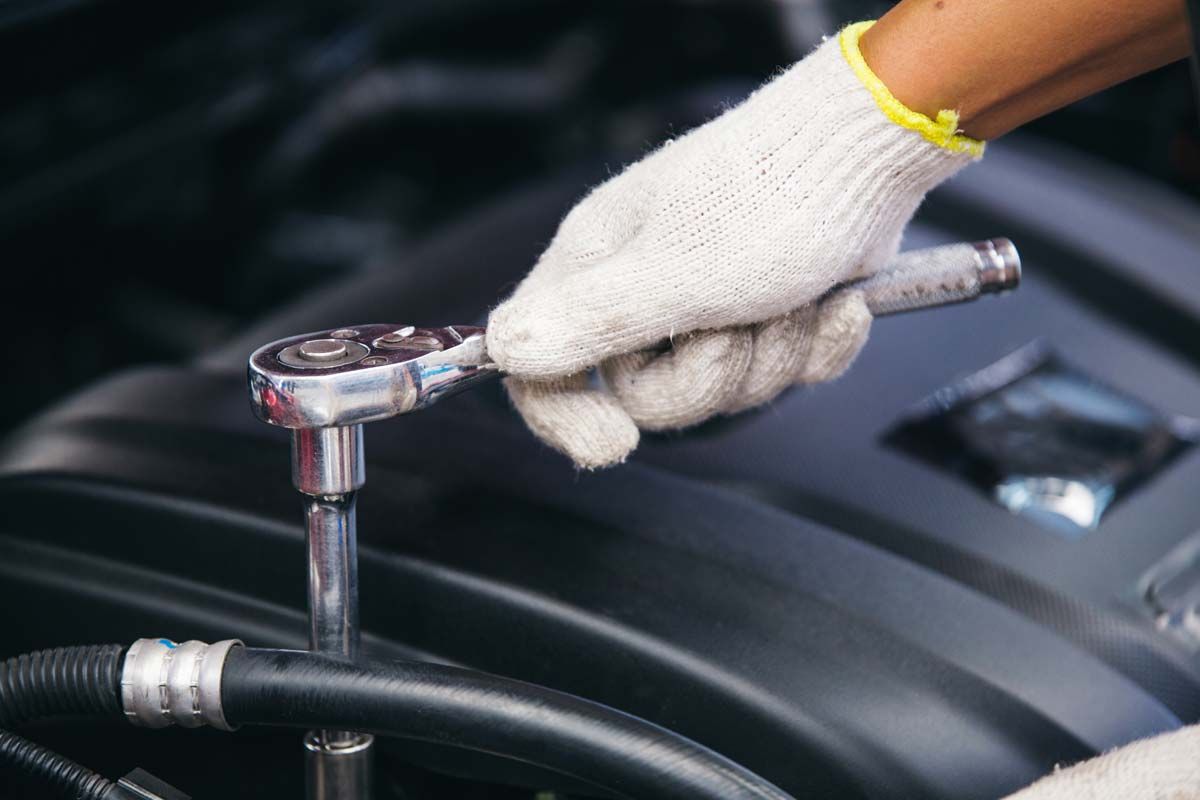 A gloved hand uses a socket wrench to work on a car engine.