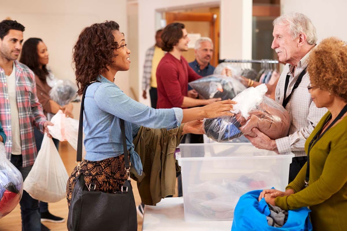 People volunteering, sorting donations in a community center. Clothing being handed over, bags and bins present.