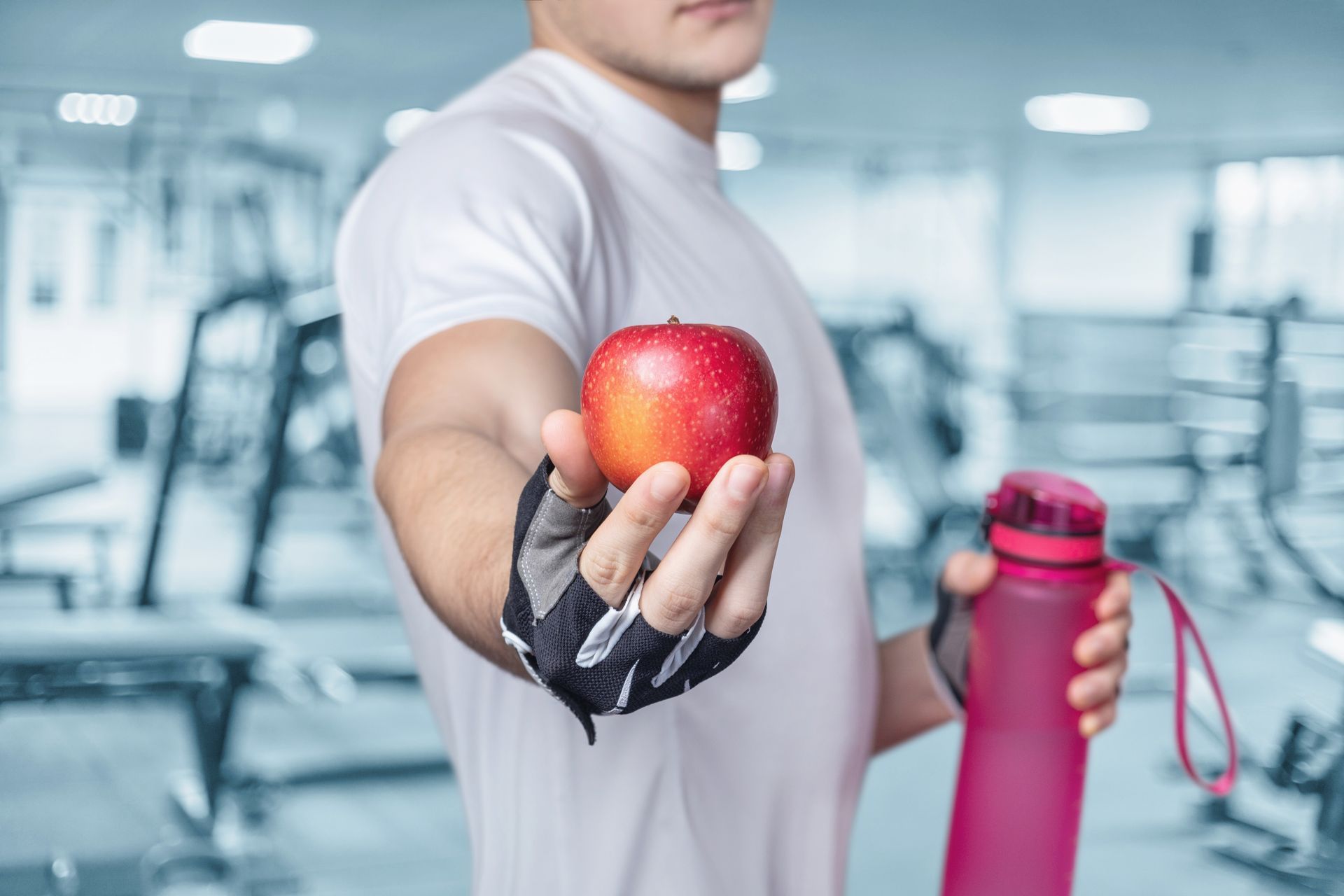 A man is holding an apple and a water bottle in a gym.