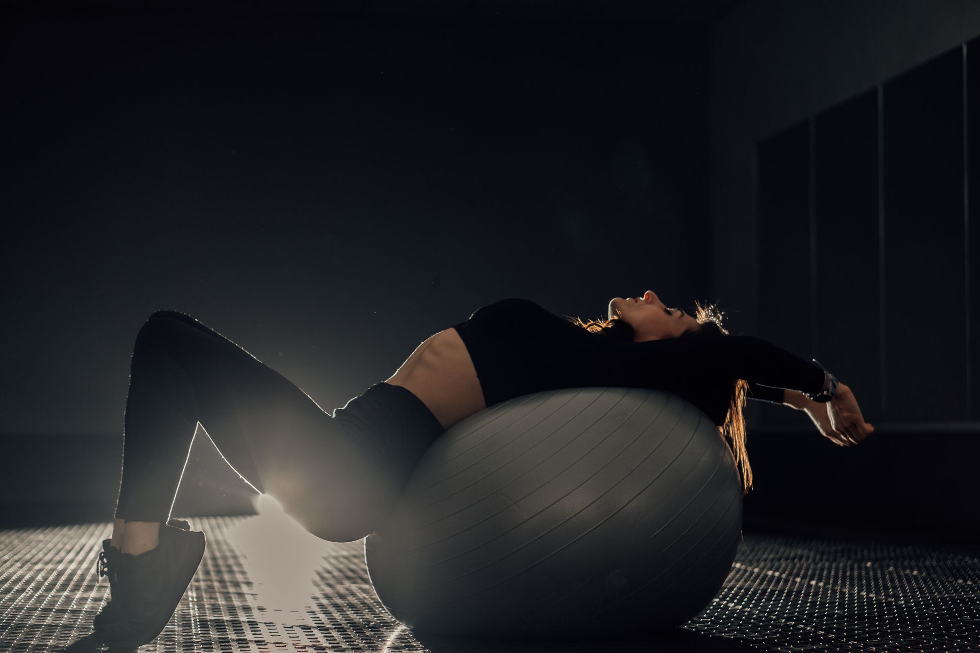 A woman is laying on a pilates ball in a dark room.