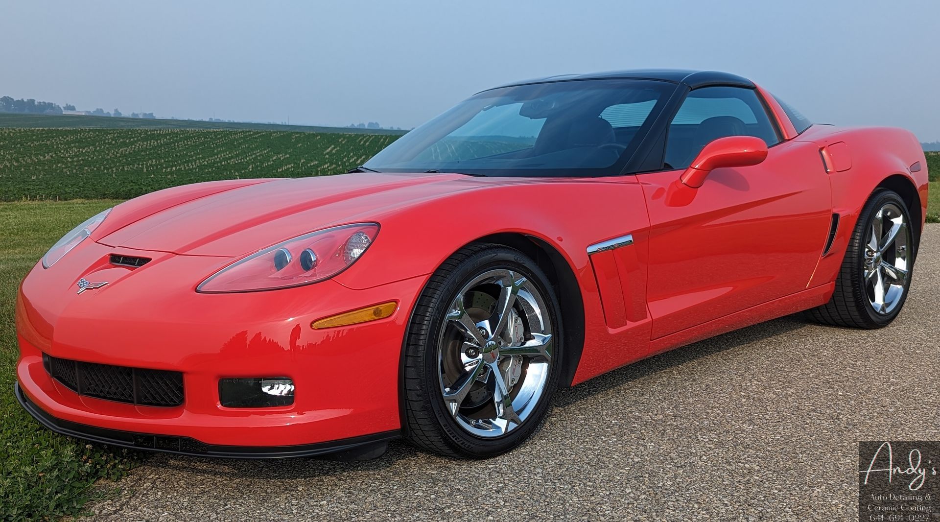 A red corvette is parked on a gravel road.