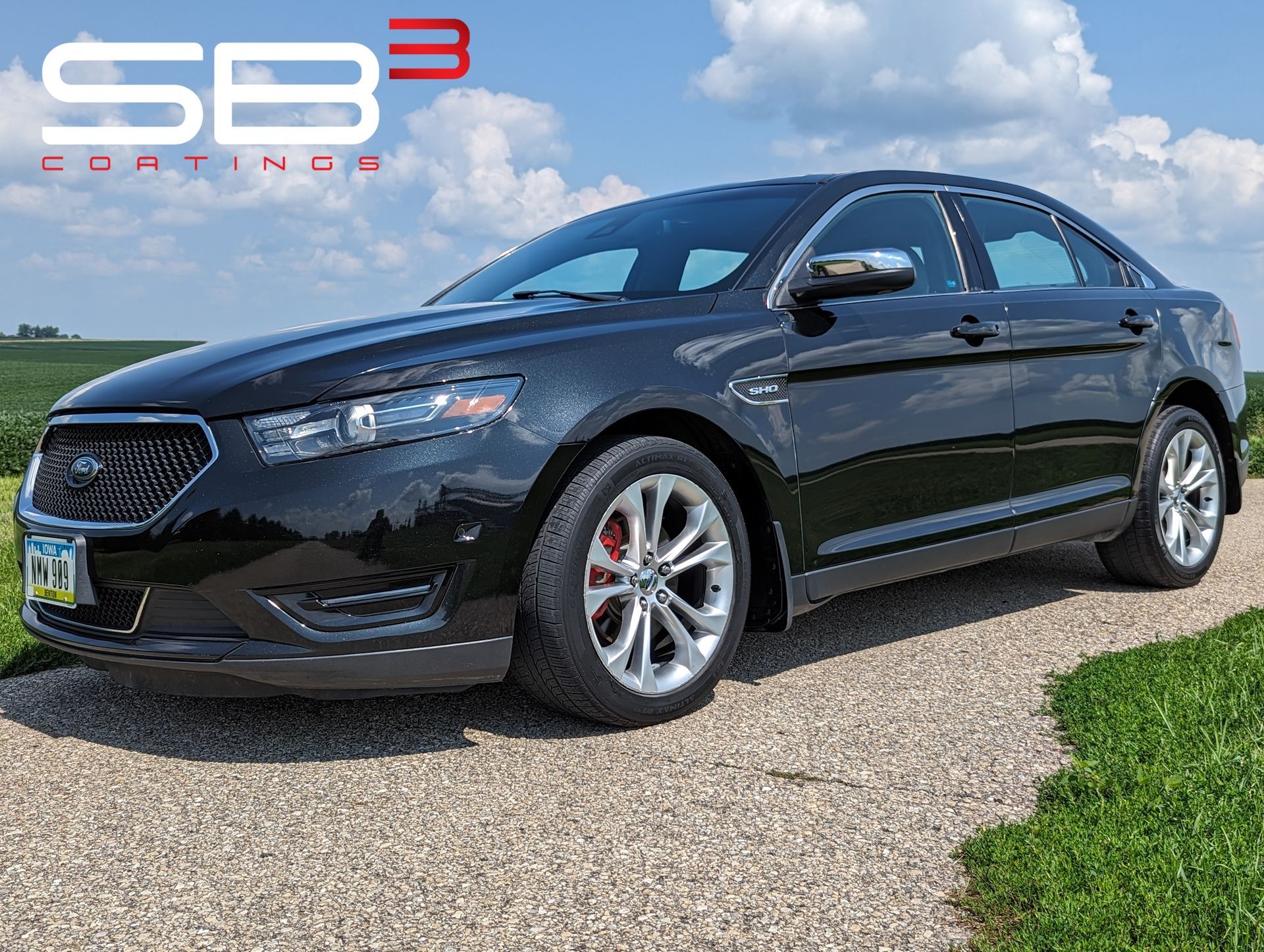 A black ford taurus is parked on a gravel road.