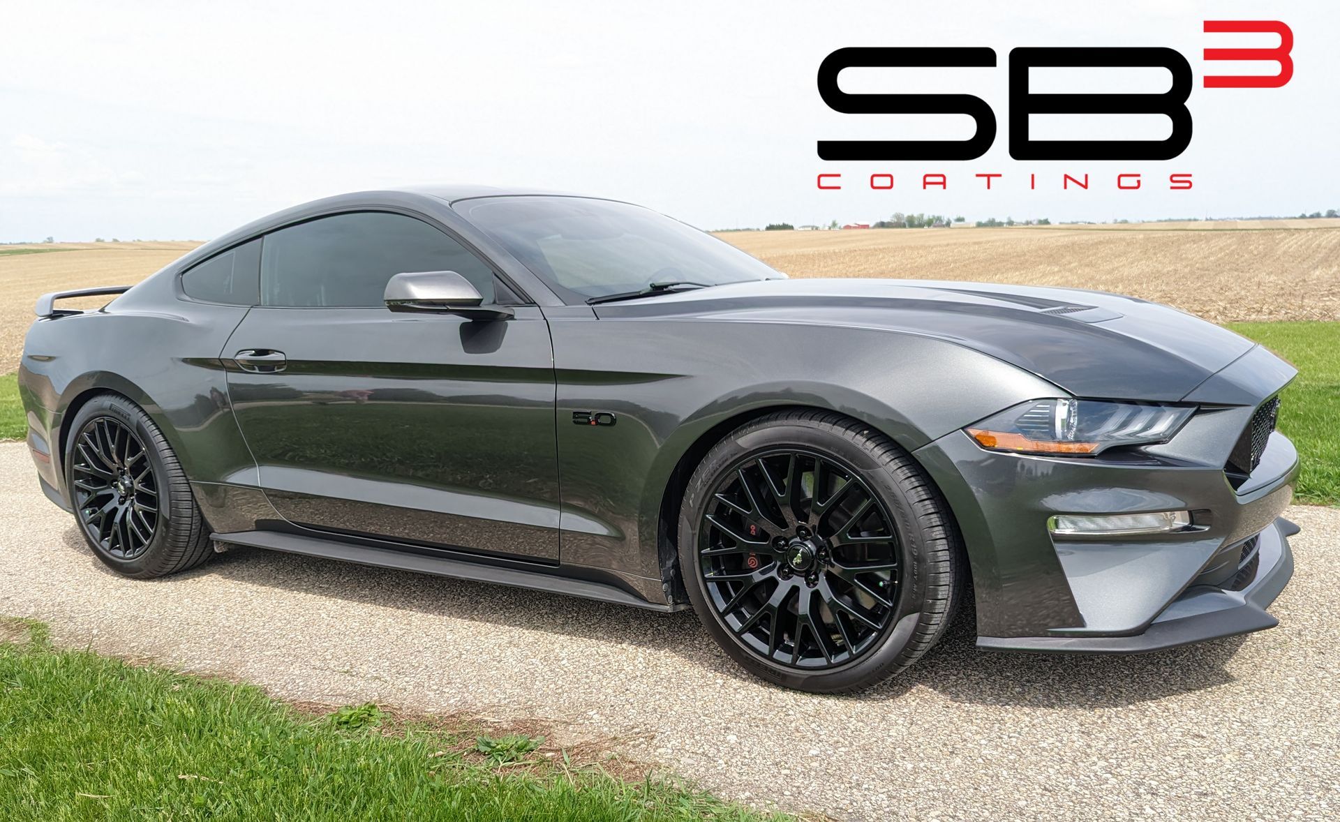 A black ford mustang is parked on a gravel road.
