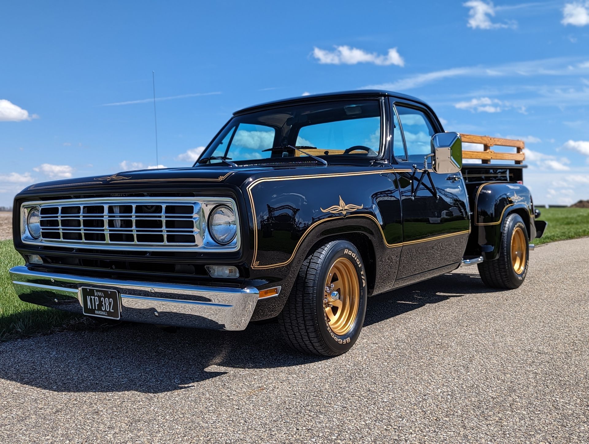 A black truck with gold wheels is parked on the side of a road.