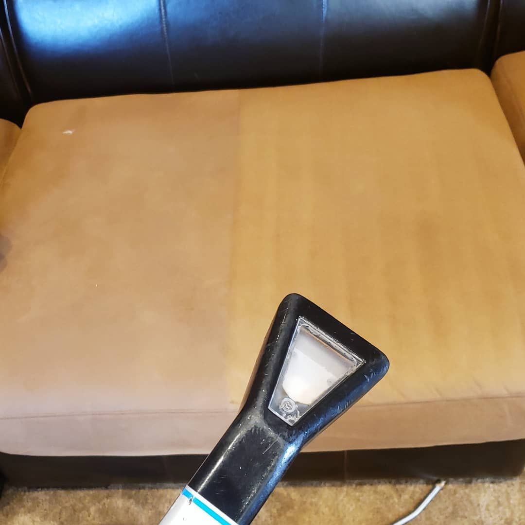 A couch is being cleaned with a vacuum cleaner