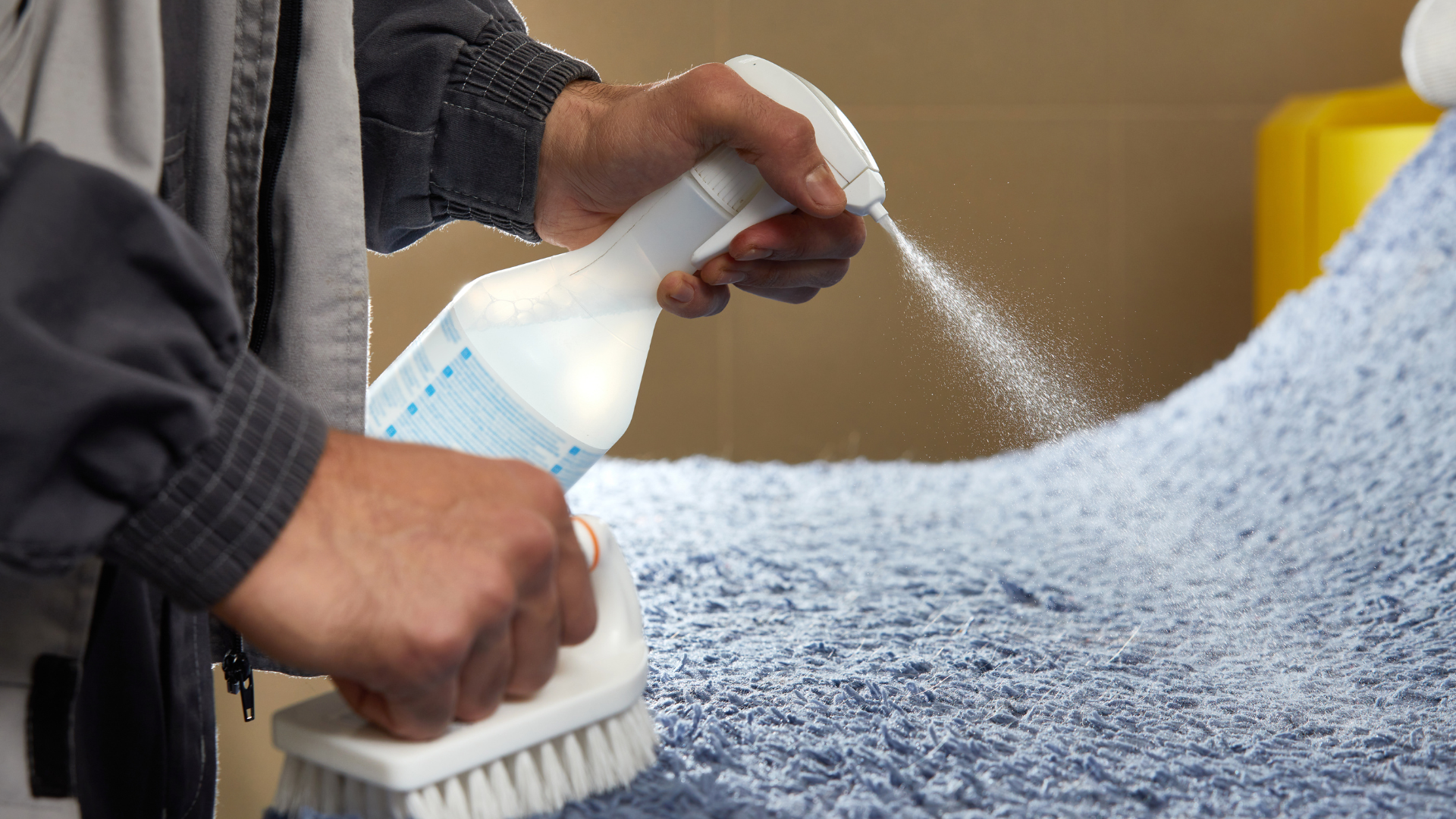 A man is cleaning a carpet with a brush and spray bottle.