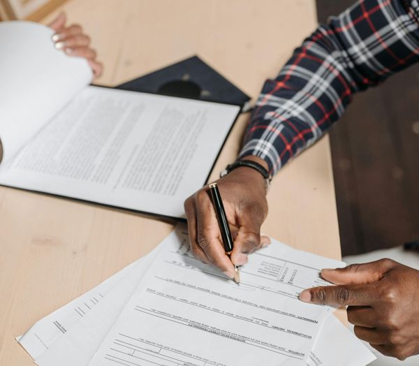 A man in a plaid shirt is signing a document with a pen.