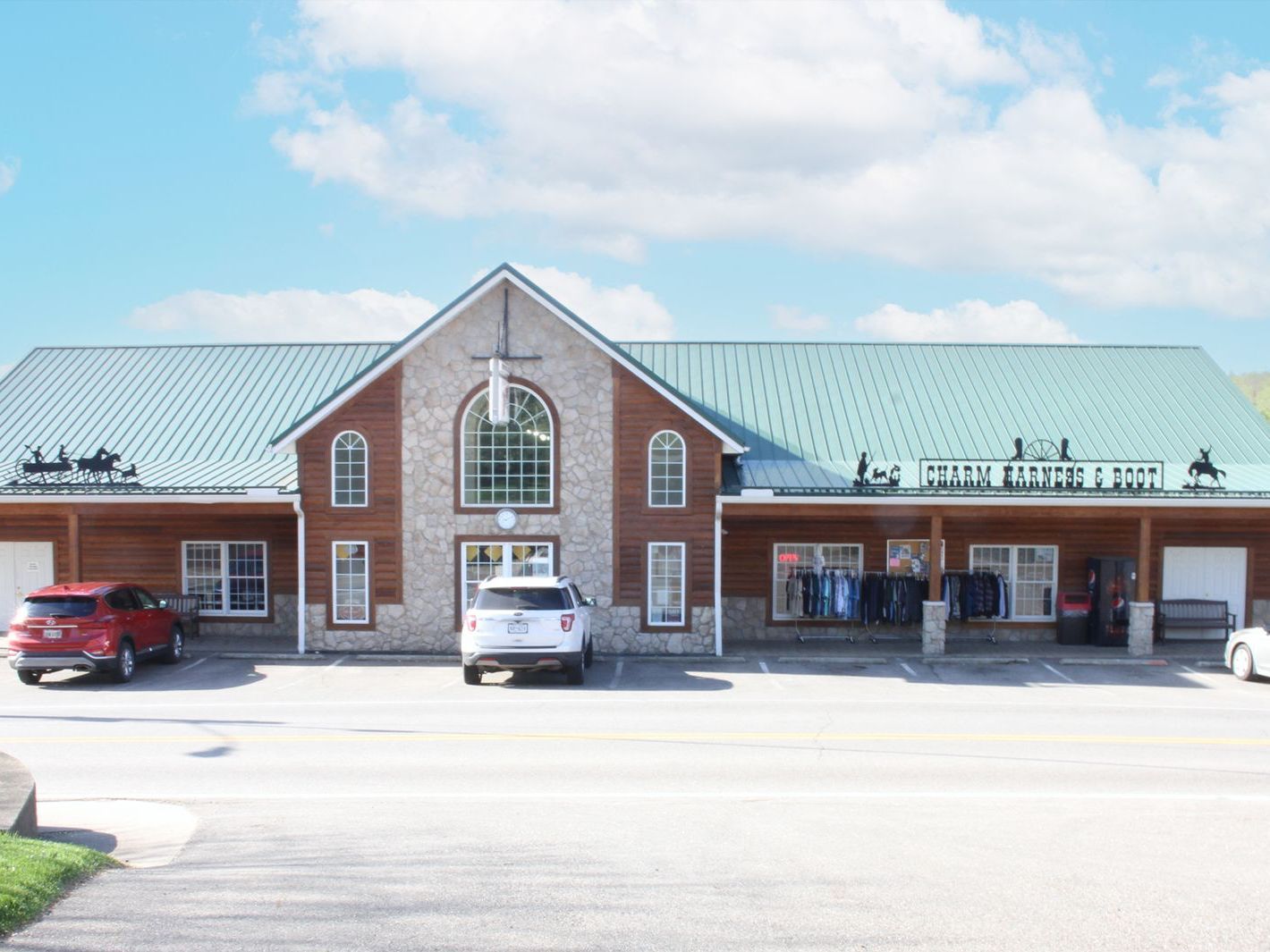 Building with brick and stone facade, green metal roof, and storefronts; cars parked in front.