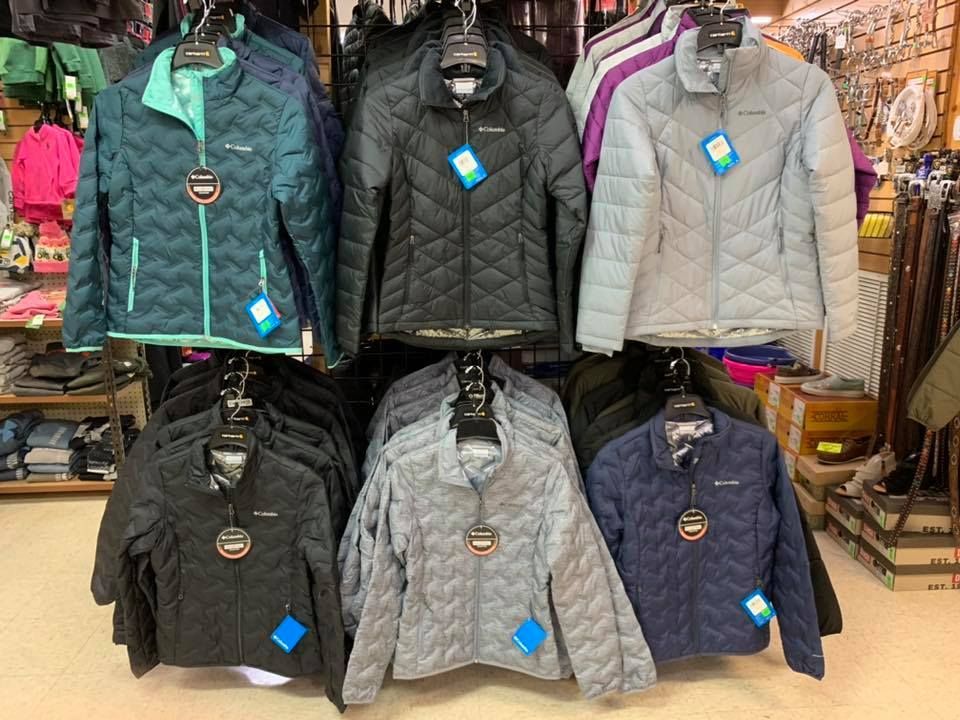 Display of Columbia puffer jackets in various colors, hanging on racks in a retail store.