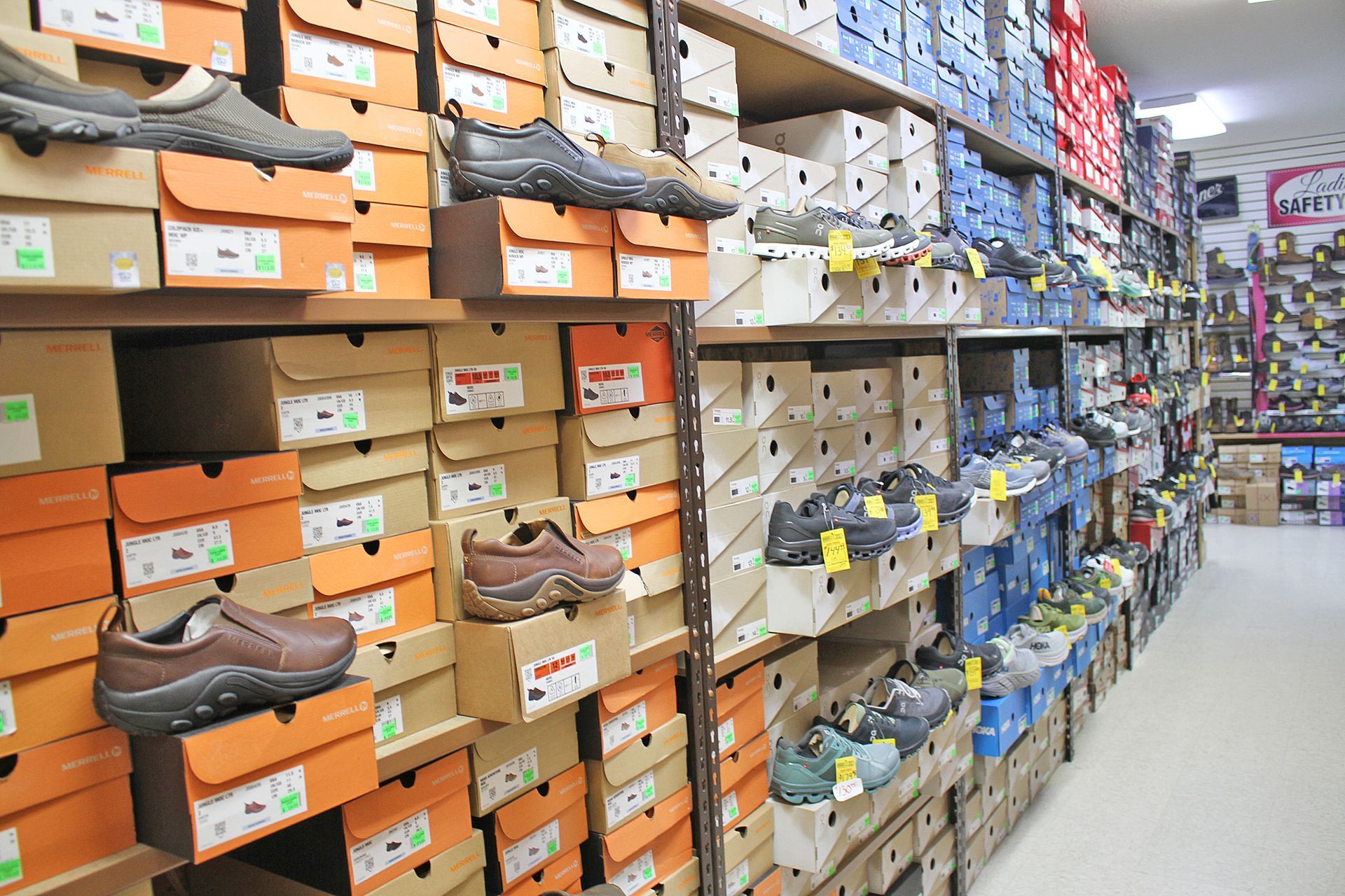 Rows of shoeboxes stacked on shelves in a retail store; some shoes are displayed on top.