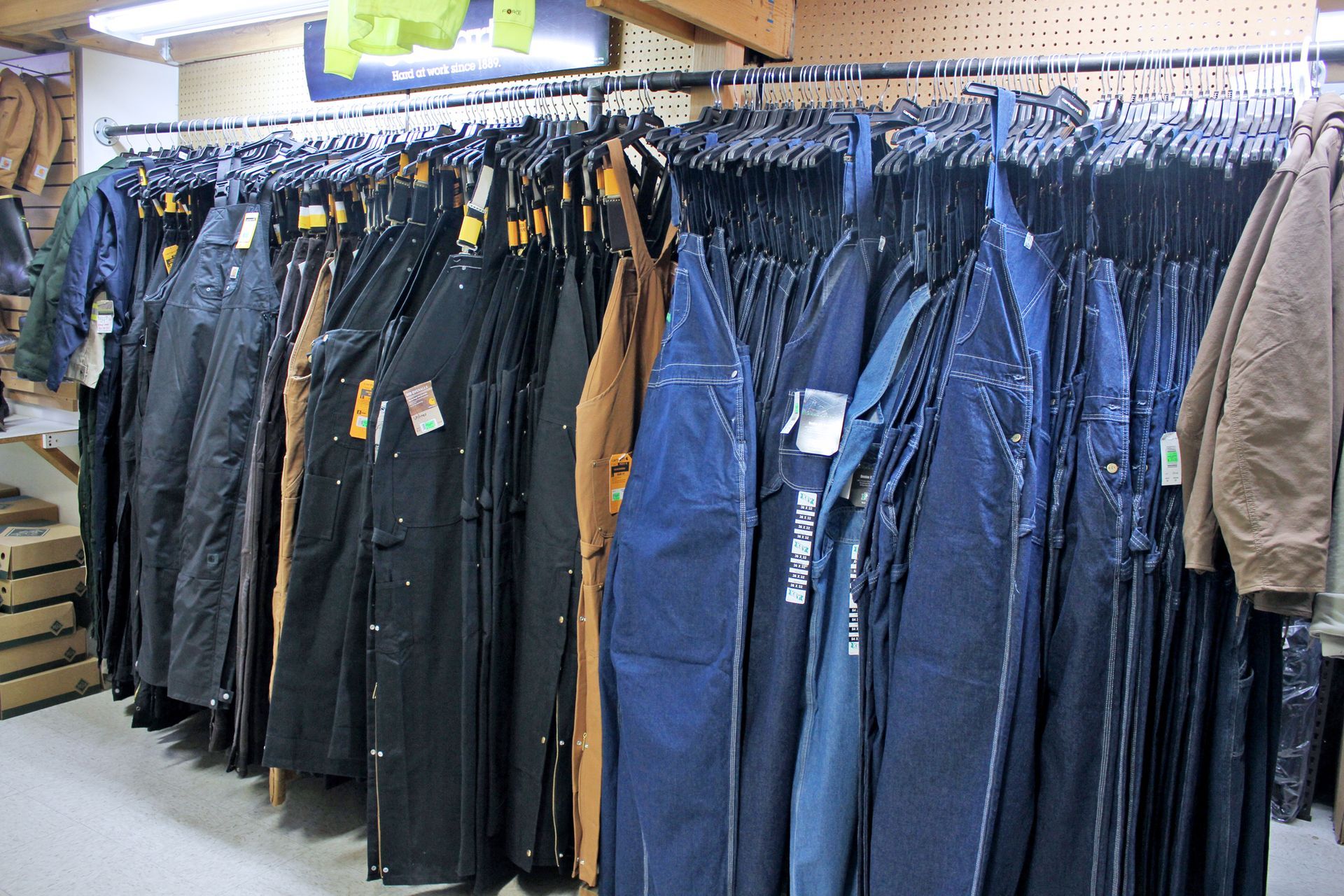 Clothing rack with workwear, including overalls and jackets, in a retail store.