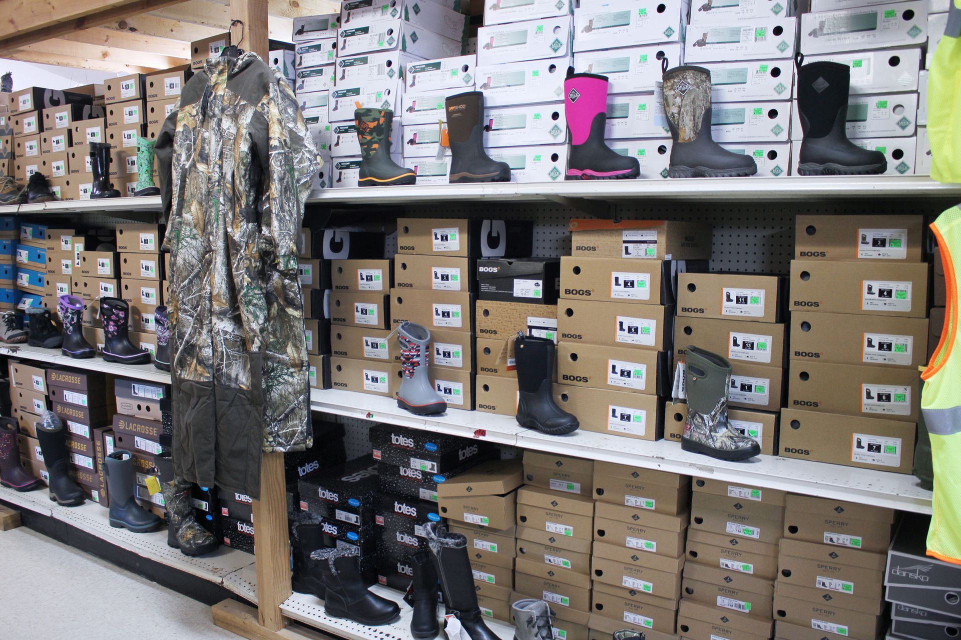 Shelves stocked with boot boxes and various boot styles; camouflage suit displayed.