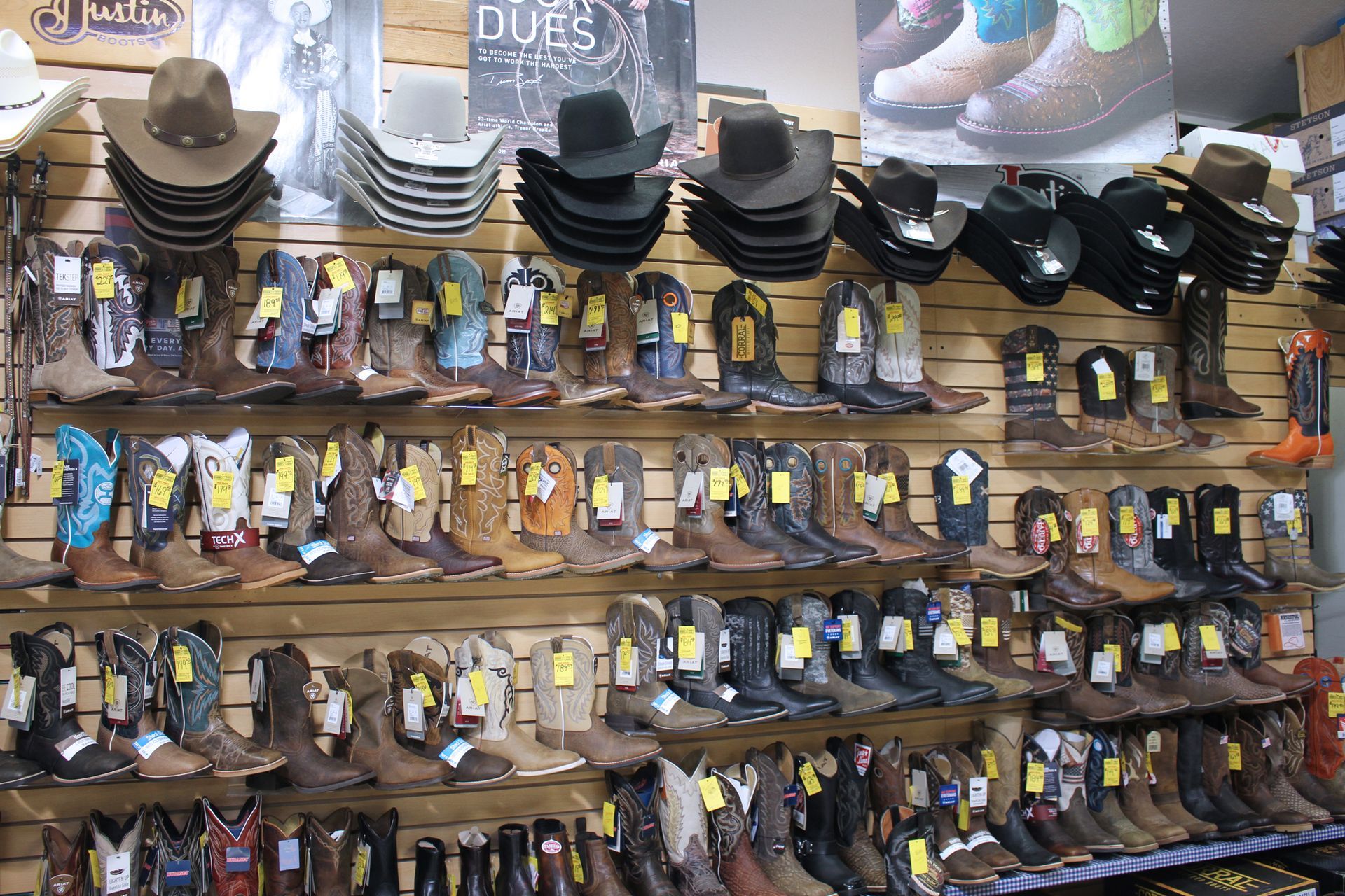 Rows of cowboy boots and hats displayed for sale on wooden shelves.