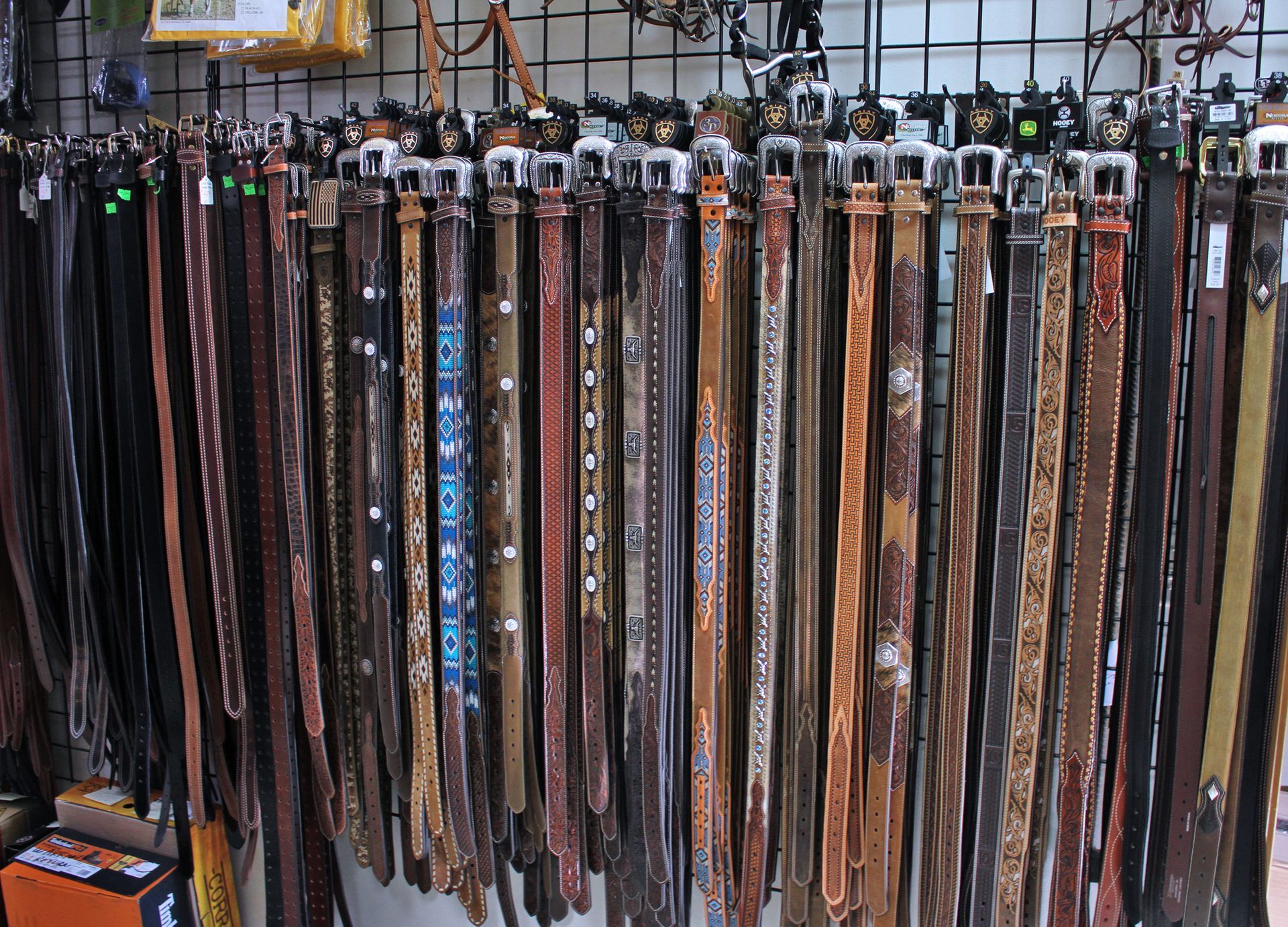 Row of leather belts of various colors and patterns displayed on a store rack.