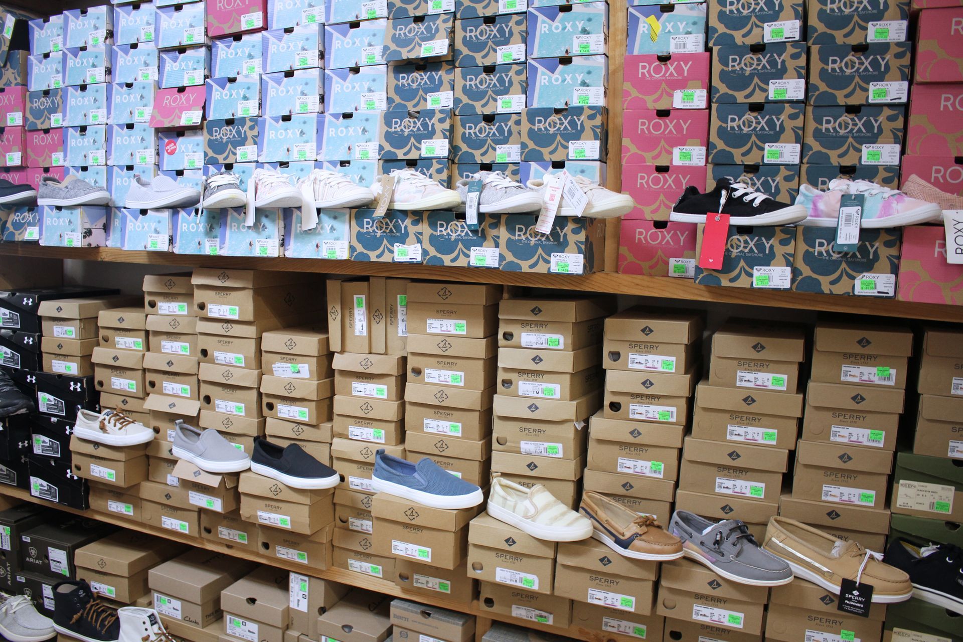 Shoes displayed on shelves in a retail store, with boxes stacked above and below.