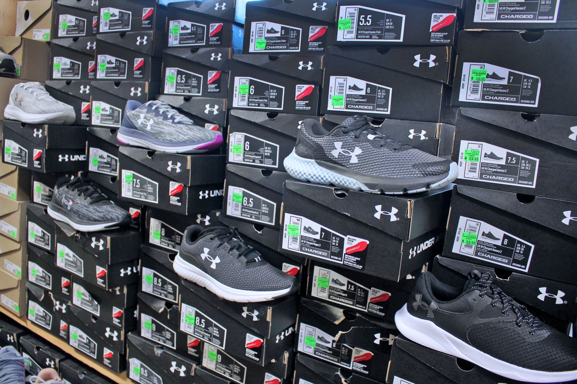 Display of Under Armour shoes stacked on top of black boxes. Various colors visible.