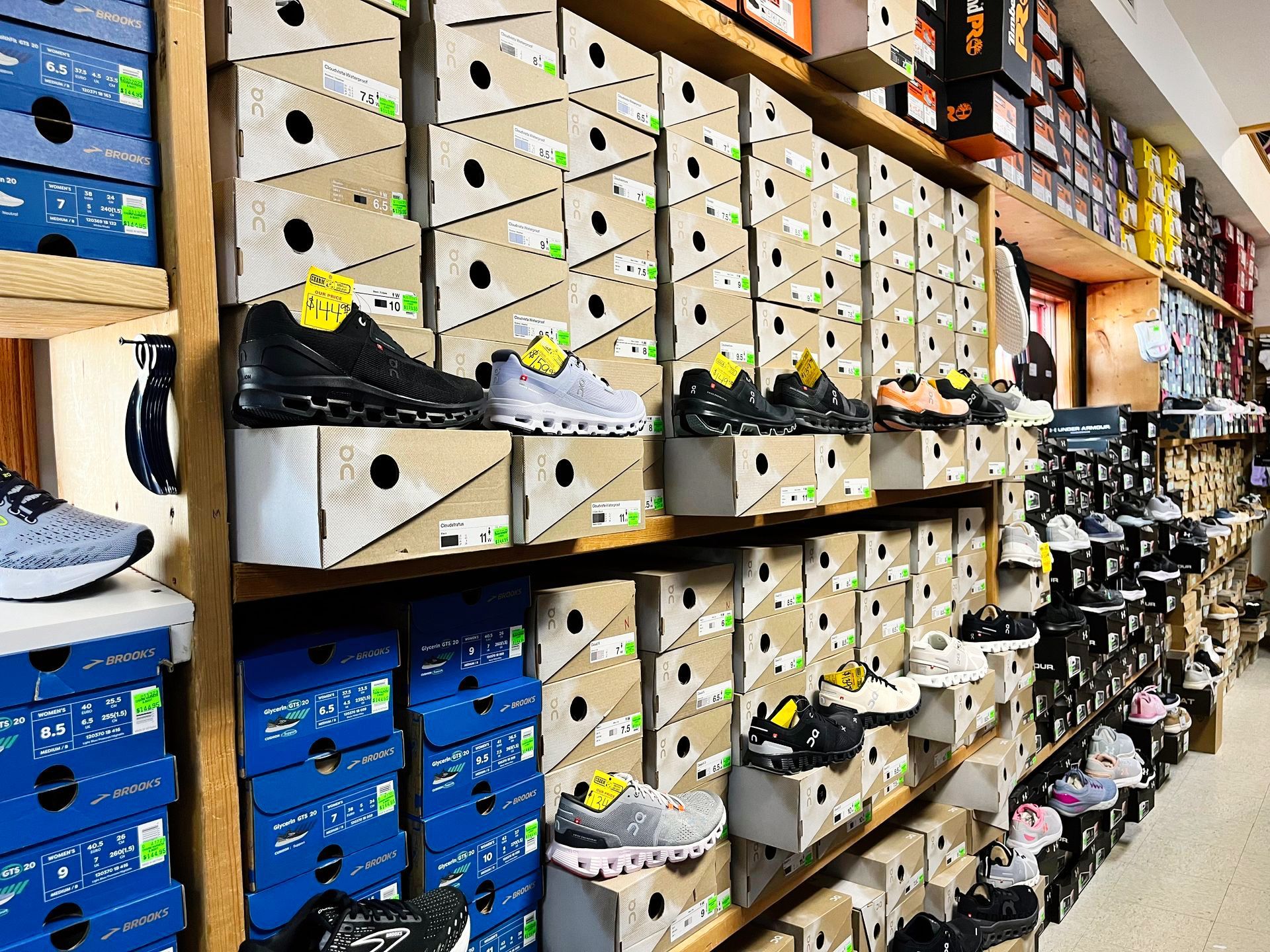 Shelves of shoe boxes in a store with some shoes displayed on top.