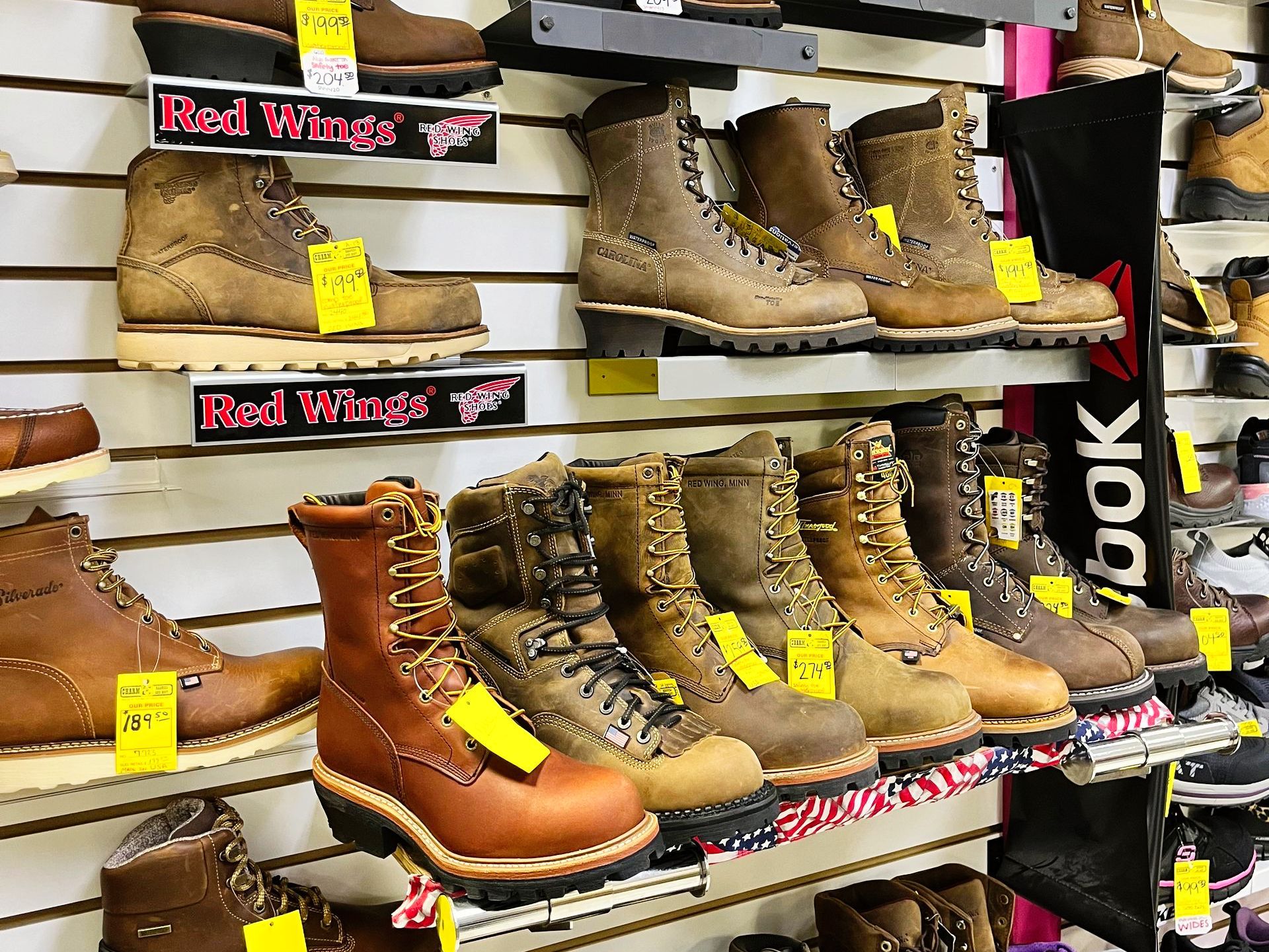 Shelves displaying various brown work boots in a store; Red Wings and Reebok brands visible.