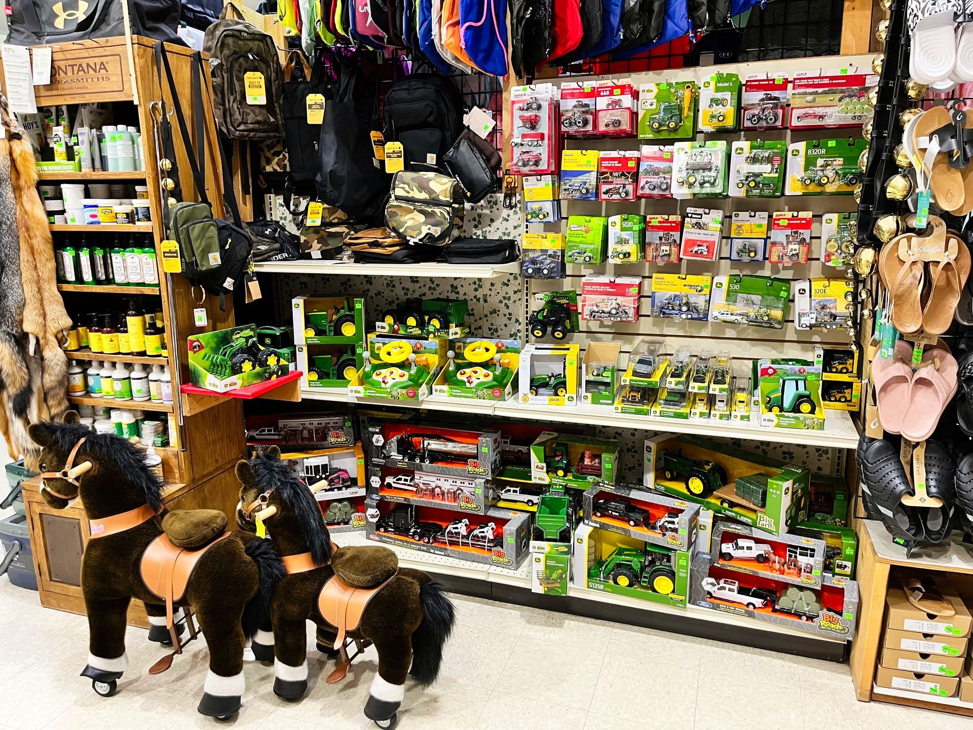 Inside a store, a display of toy tractors, accessories, and hobby horses.