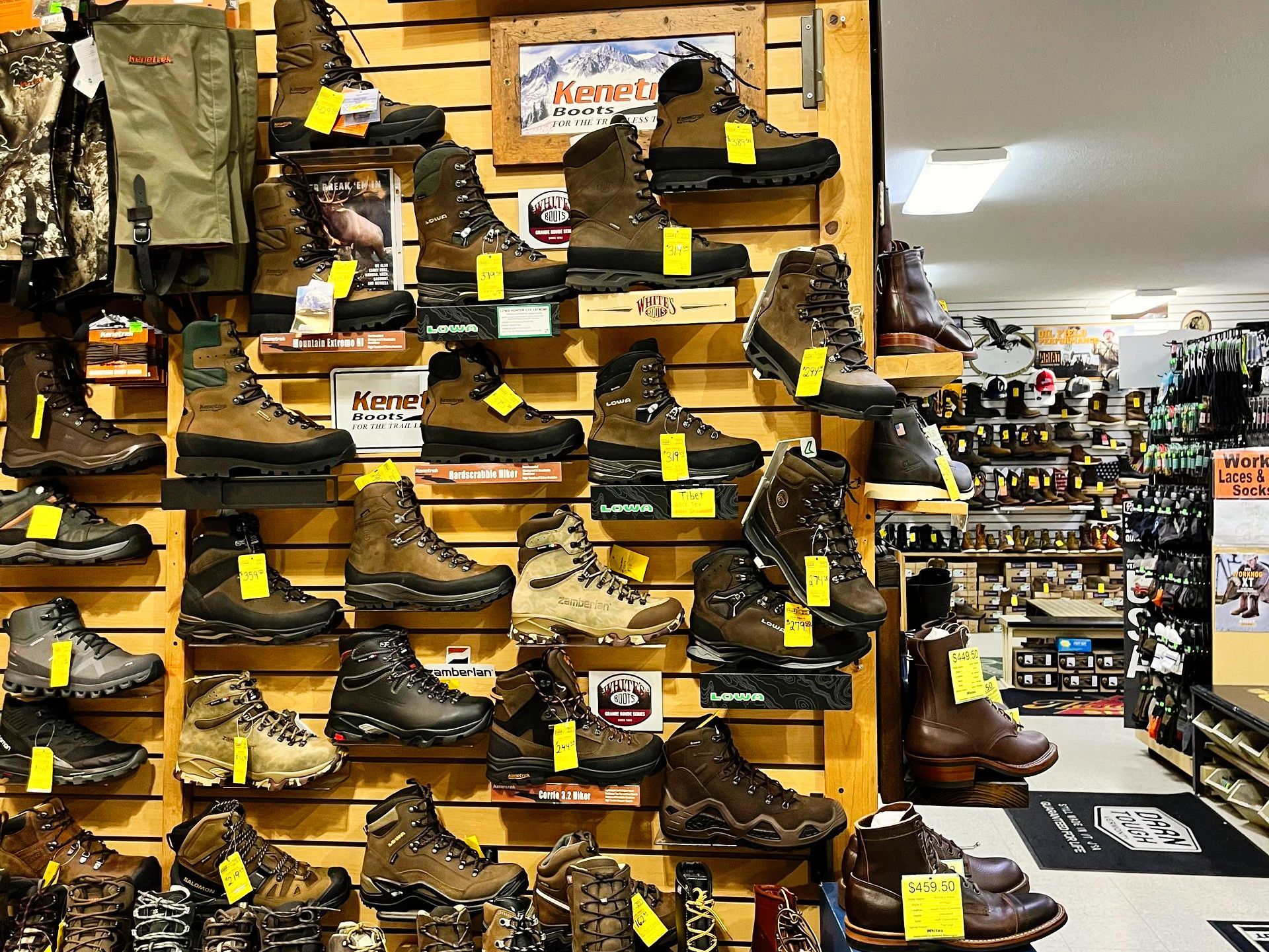 Wall display in a store, filled with various hiking and work boots, all with price tags.