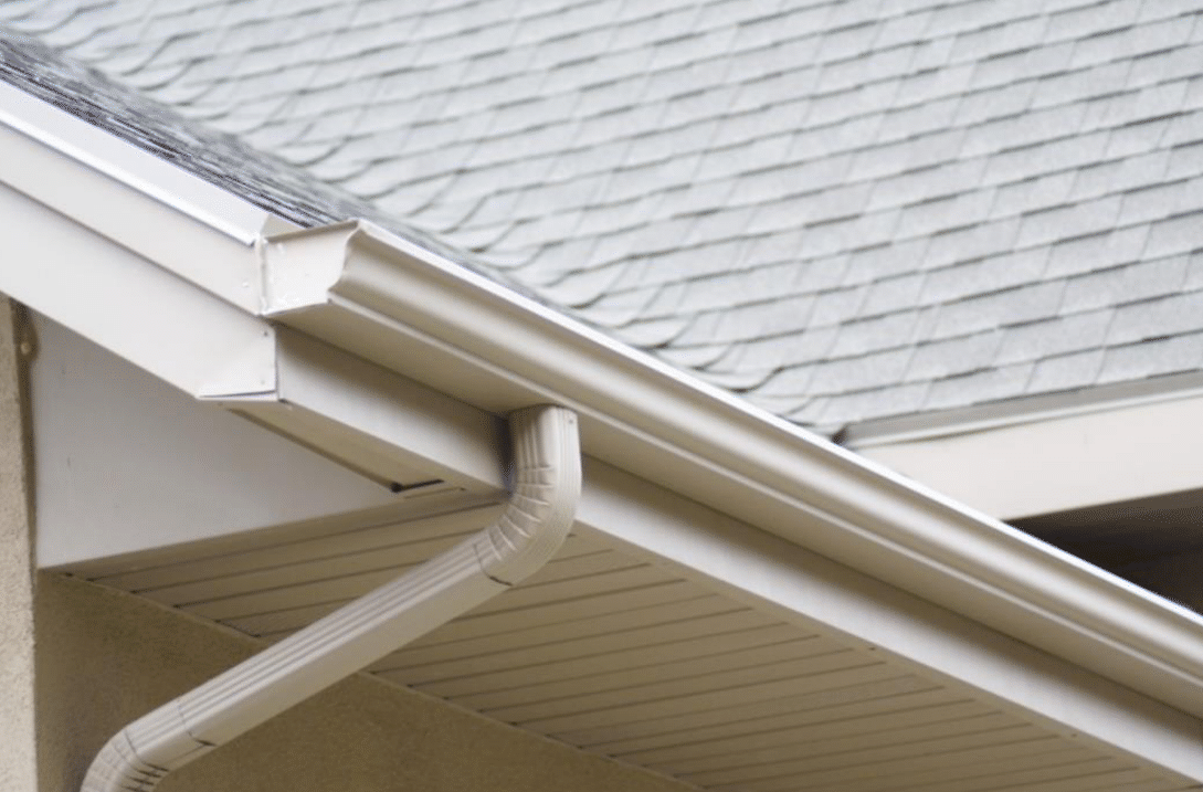Beige rain gutter attached to a house roof.