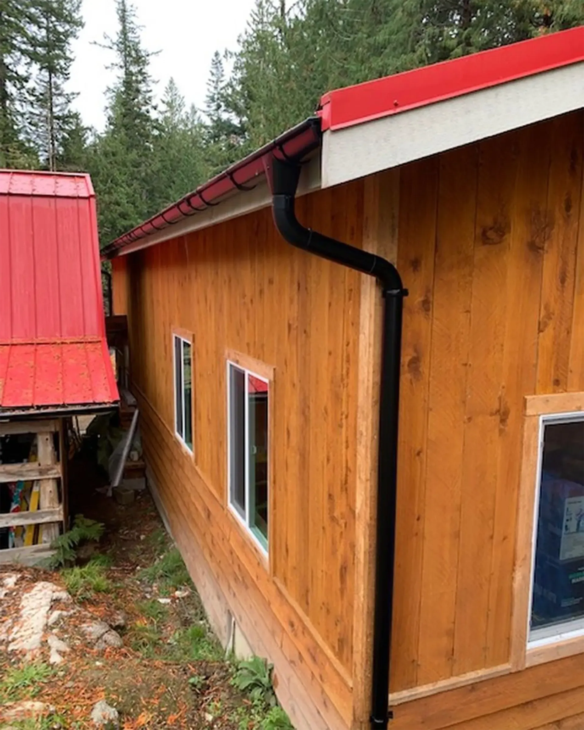 Wooden building with red roof, black gutter and downspout, and white-framed windows.