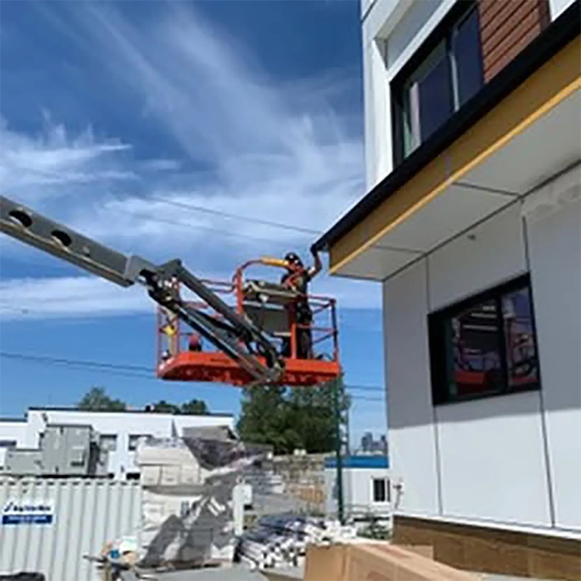 Construction worker in an aerial lift installing roofing on a building; sunny day.