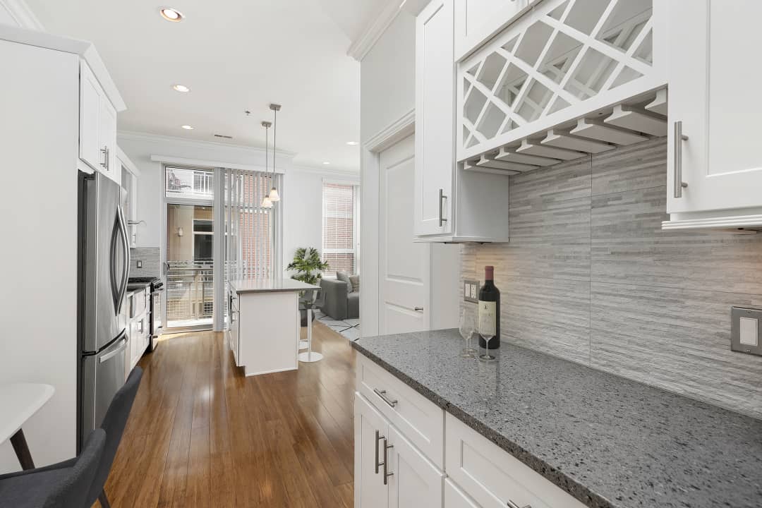 A kitchen with white cabinets, granite countertops, a wine rack, and a bottle of wine on the counter at Reside on Jackson.