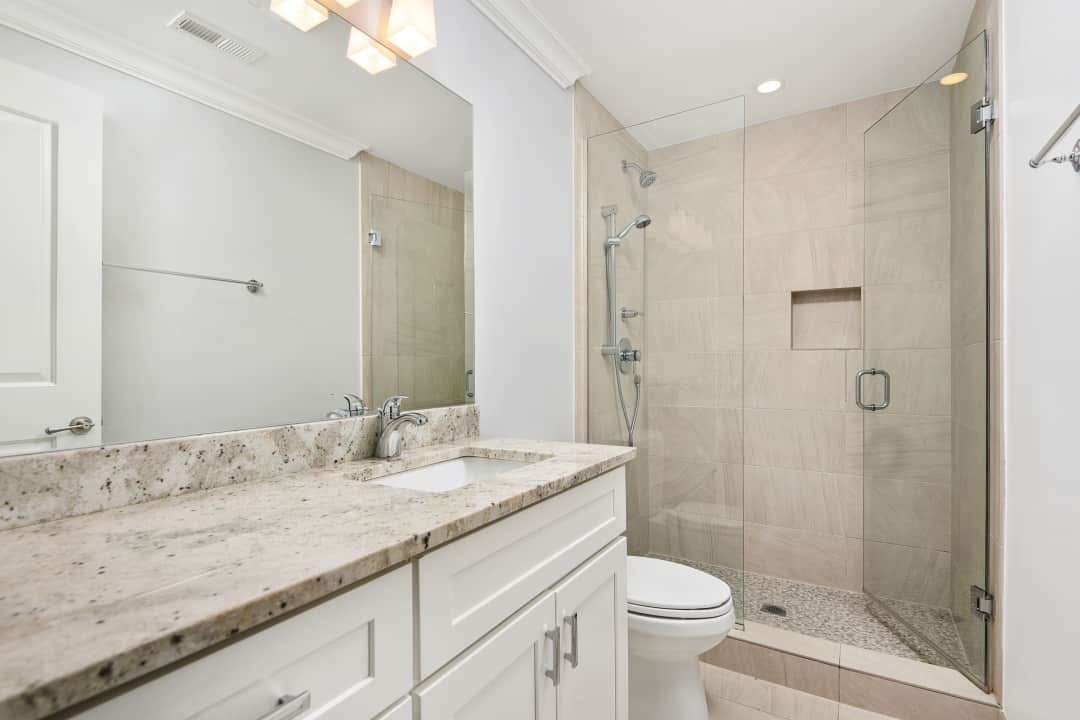 A bathroom with a toilet, sink, mirror, and walk-in shower at Reside on Jackson.