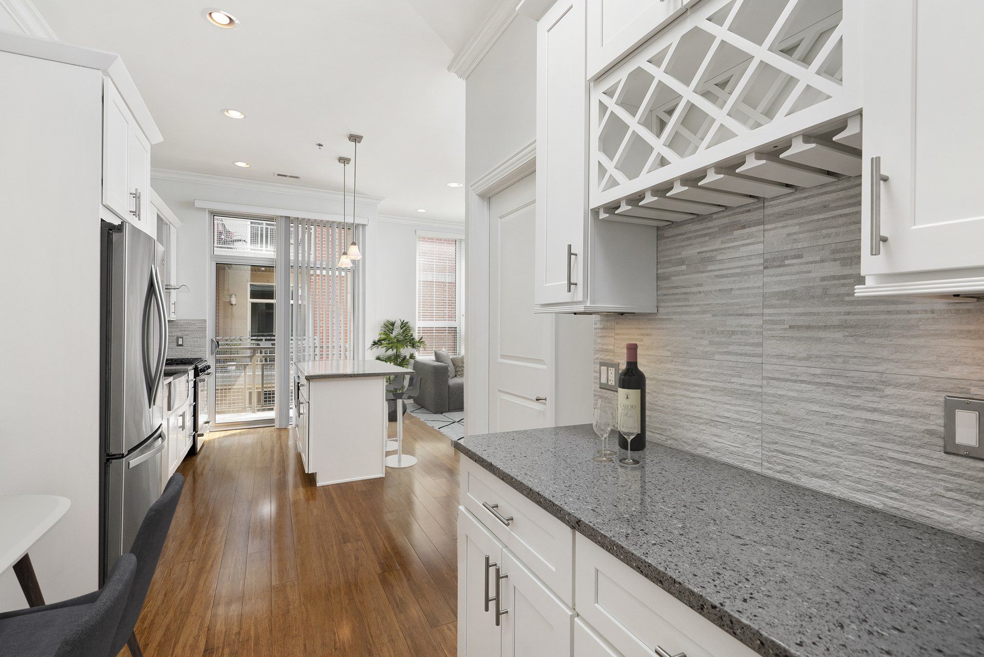 A kitchen with white cabinets, granite countertops, a wine rack, and a bottle of wine on the counter at Reside on Jackson.