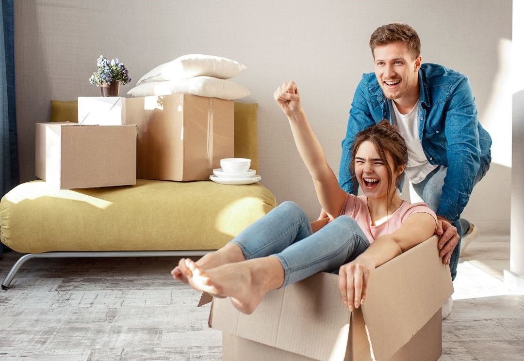 A man is kneeling next to a woman sitting in a cardboard box.