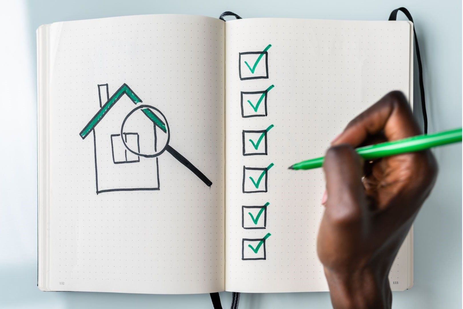 A person is drawing a house and a magnifying glass in a notebook.