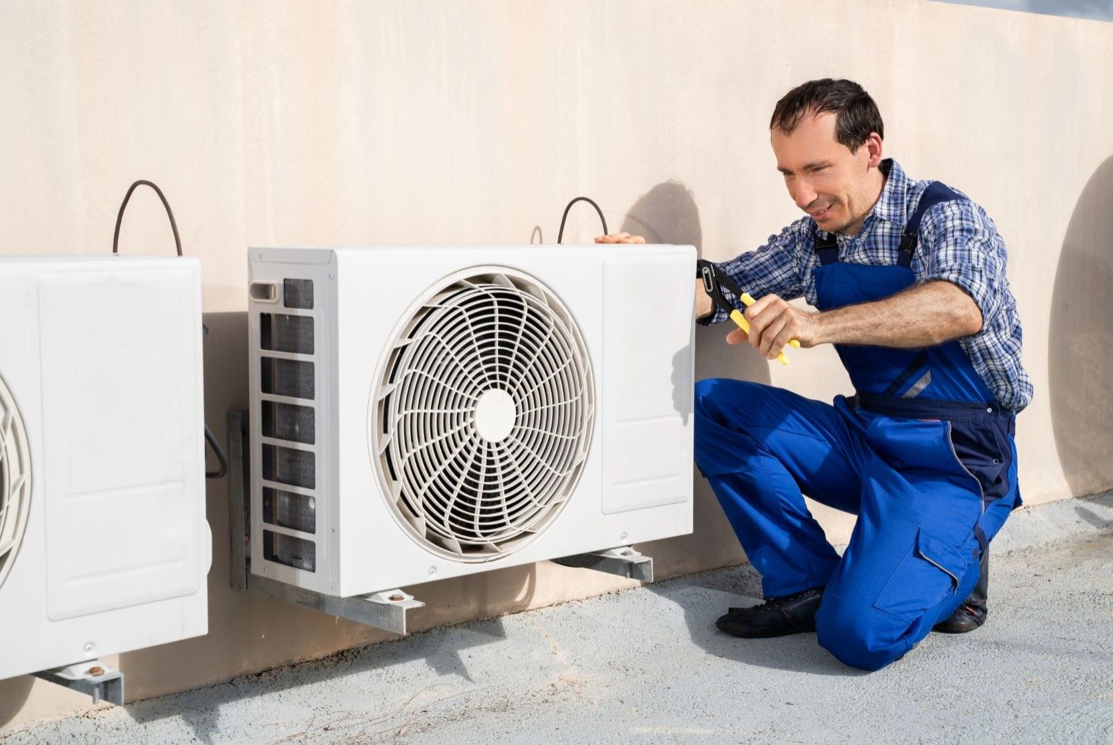 A man in blue overalls is working on an air conditioner.