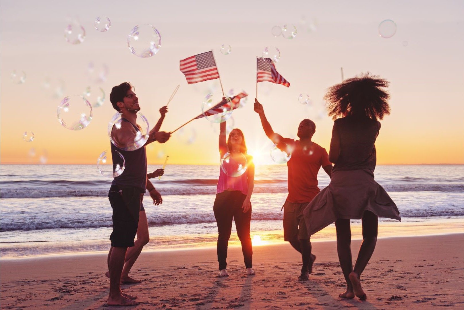 A group of people are standing on a beach holding american flags and blowing soap bubbles.