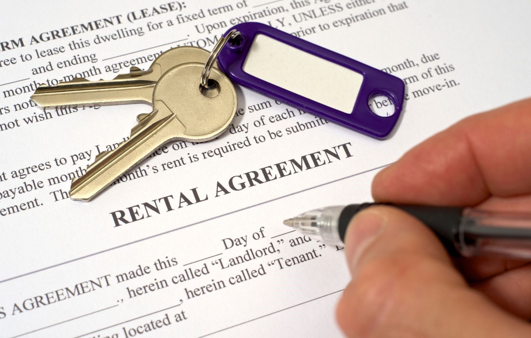 A person is signing a rental agreement with keys in the background.