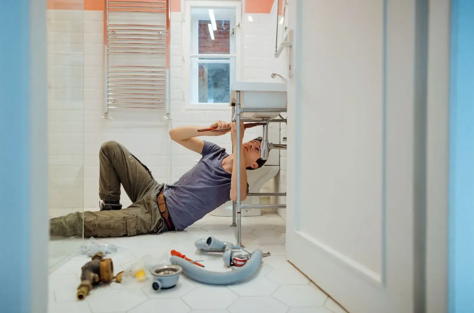 A man is laying on the floor fixing a sink in a bathroom.