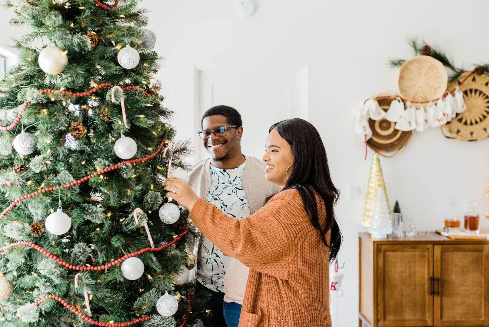 A man and a woman are decorating a christmas tree in a living room.