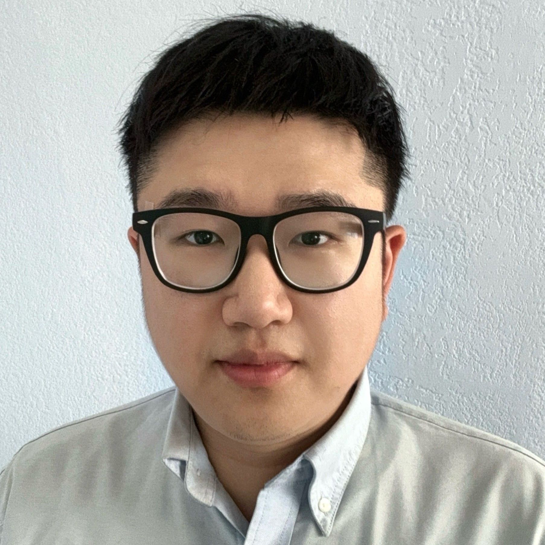 A young man wearing glasses and a grey shirt is looking at the camera.