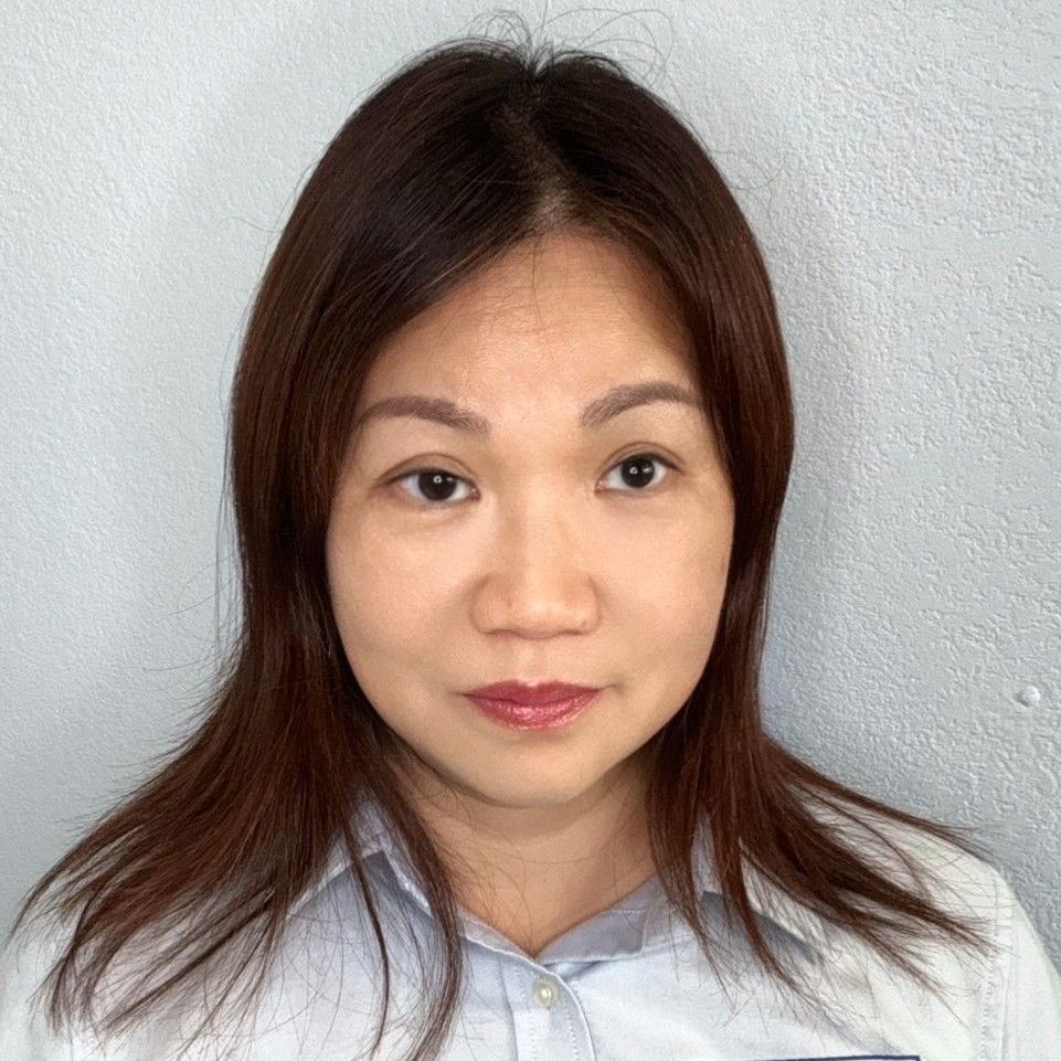 A woman with long brown hair is wearing a white shirt and looking at the camera.
