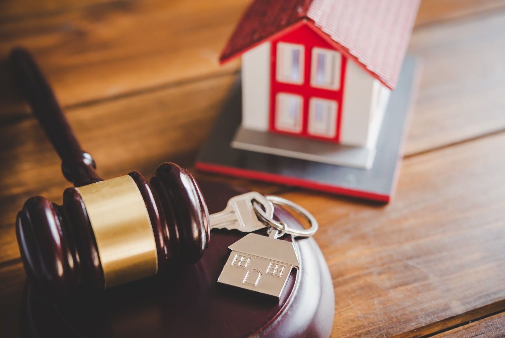 A judge 's gavel , keys and a model house on a wooden table.