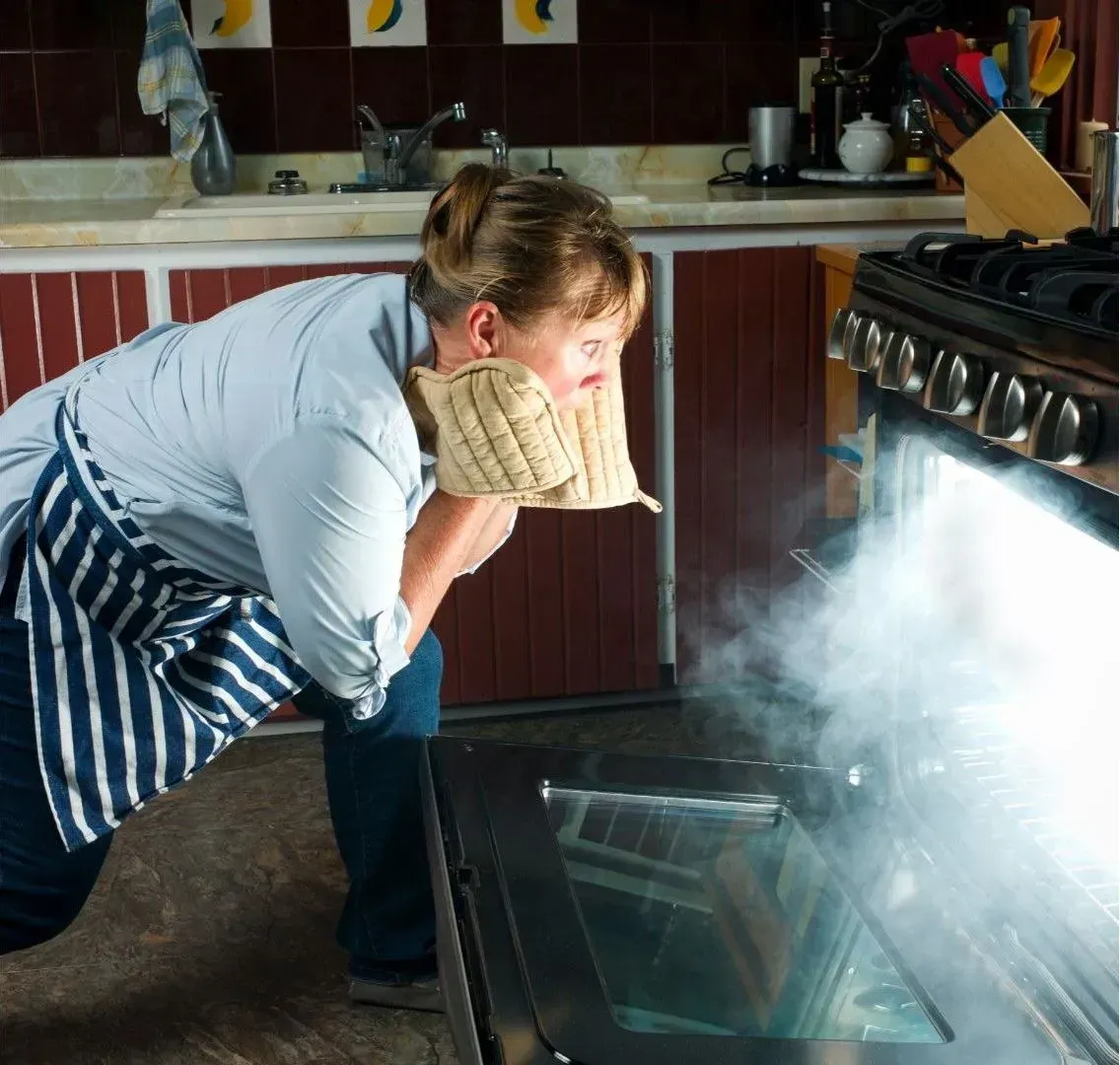 A woman is looking into an oven with steam coming out of it