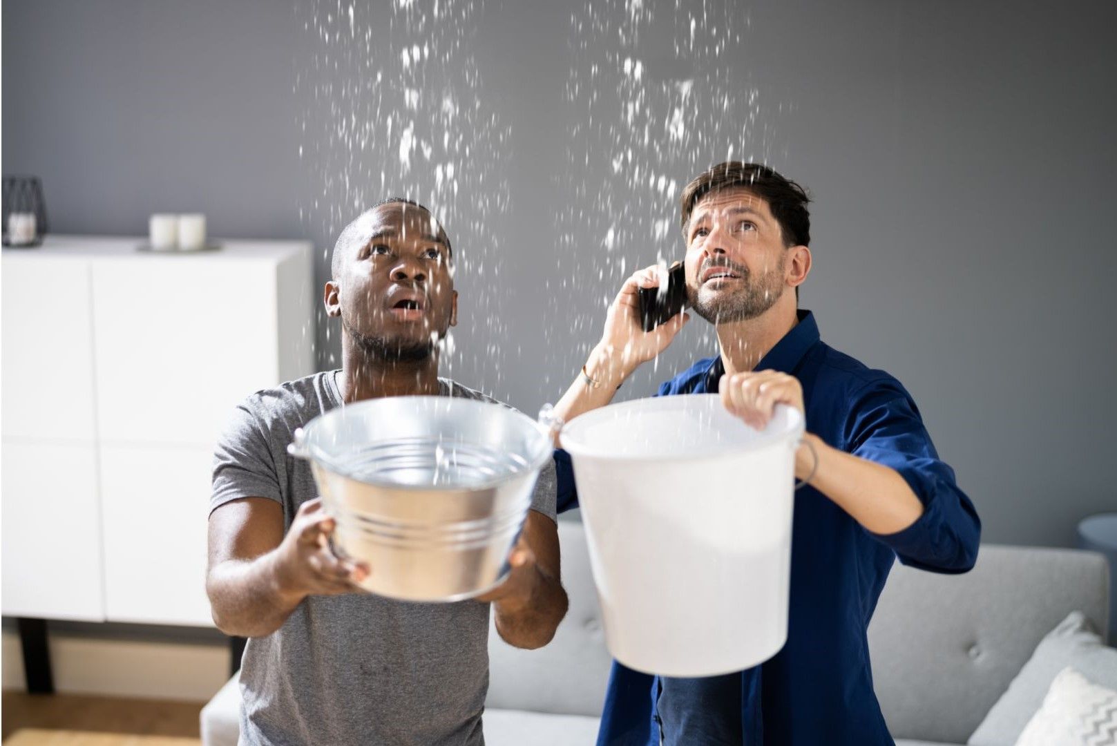 Two men are holding buckets of water and talking on cell phones.