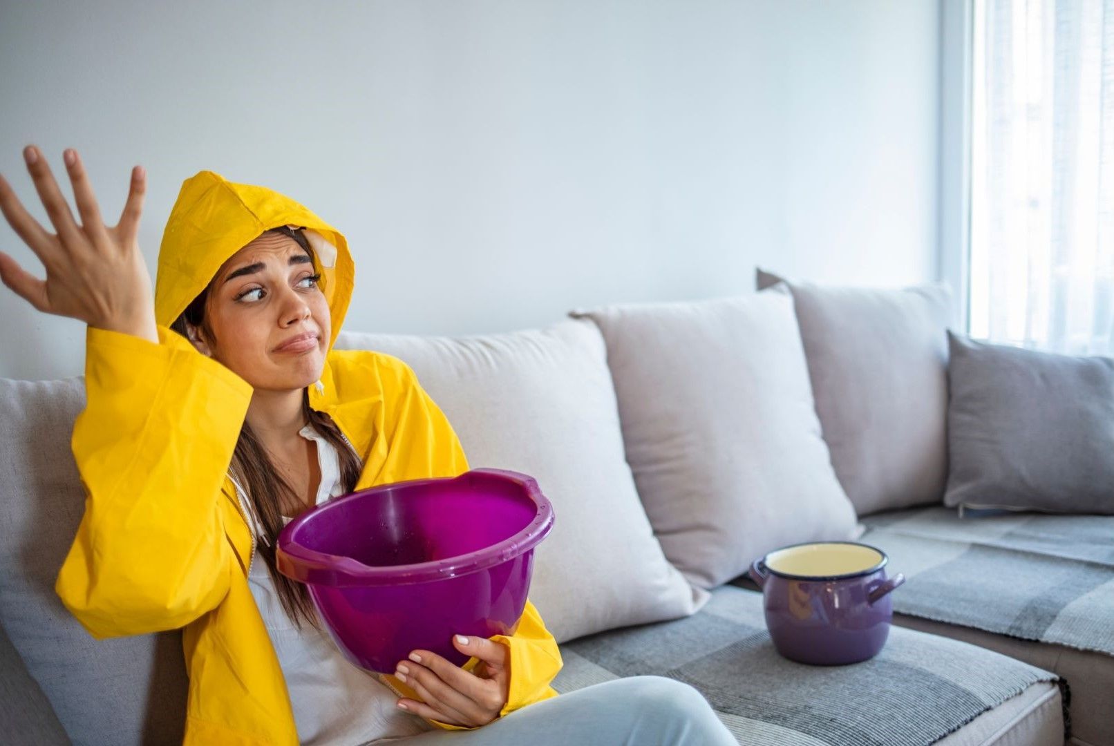 A woman in a yellow raincoat is sitting on a couch holding a purple bowl.