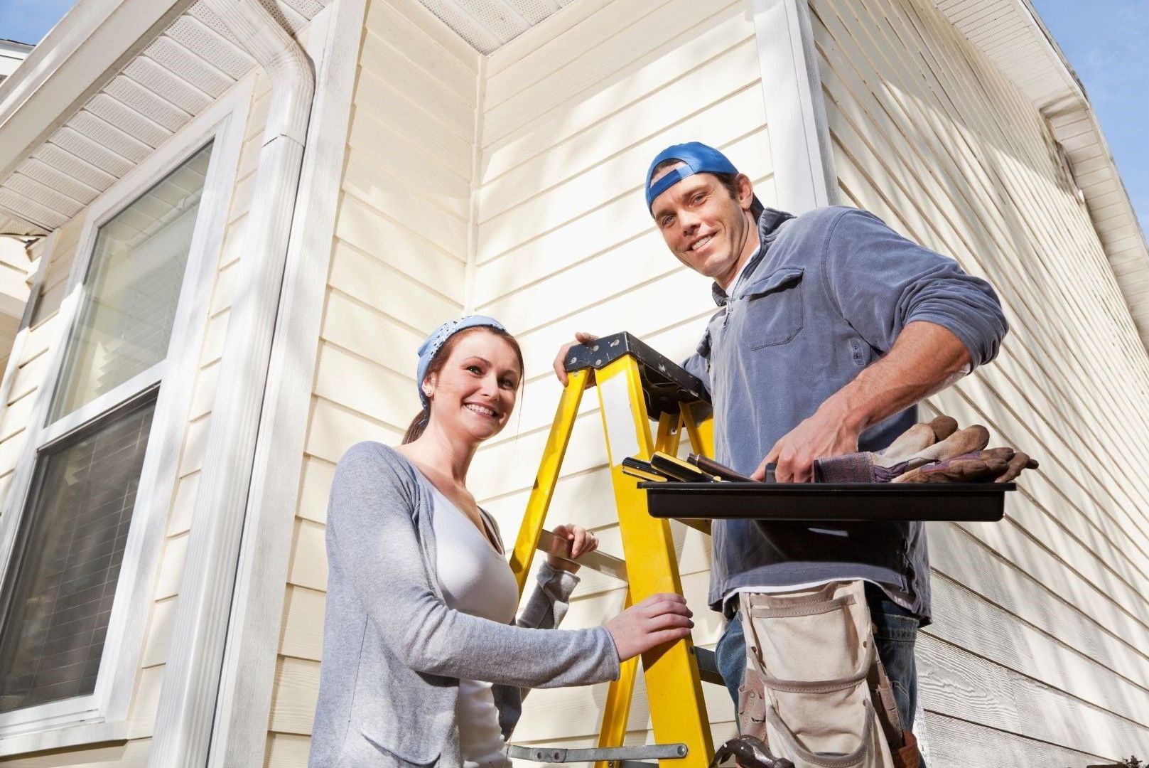 A man and a woman are standing in front of a house with a ladder.