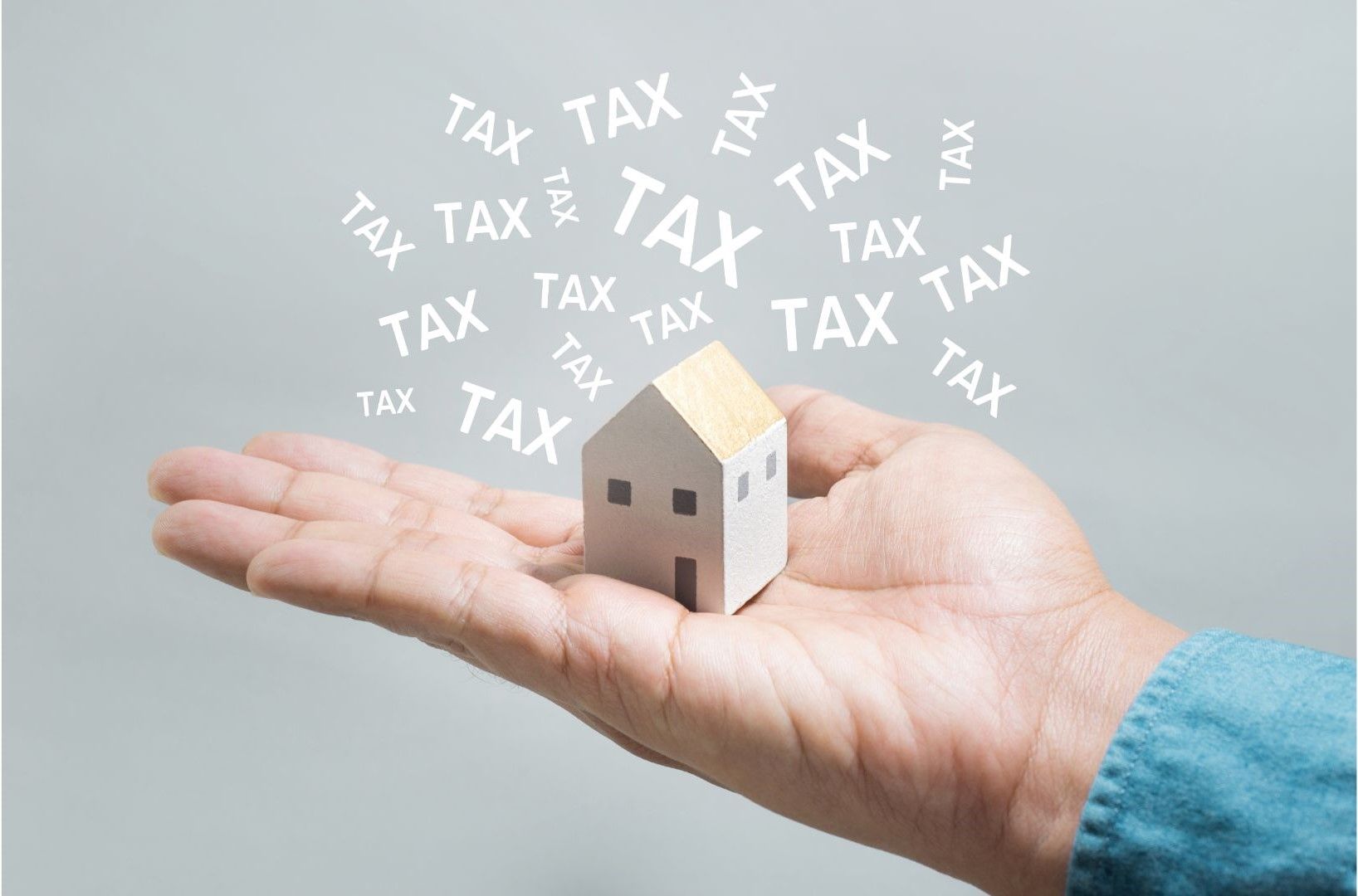 A person is holding a small house in their hand surrounded by taxes.