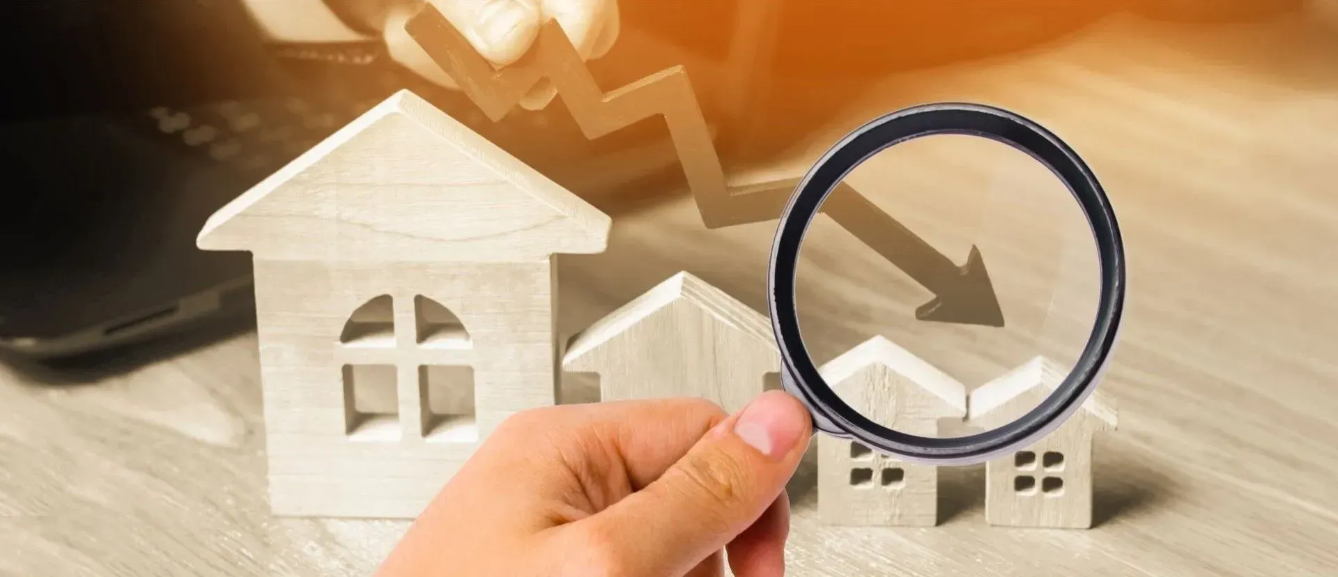 A person is holding a magnifying glass over a model house.
