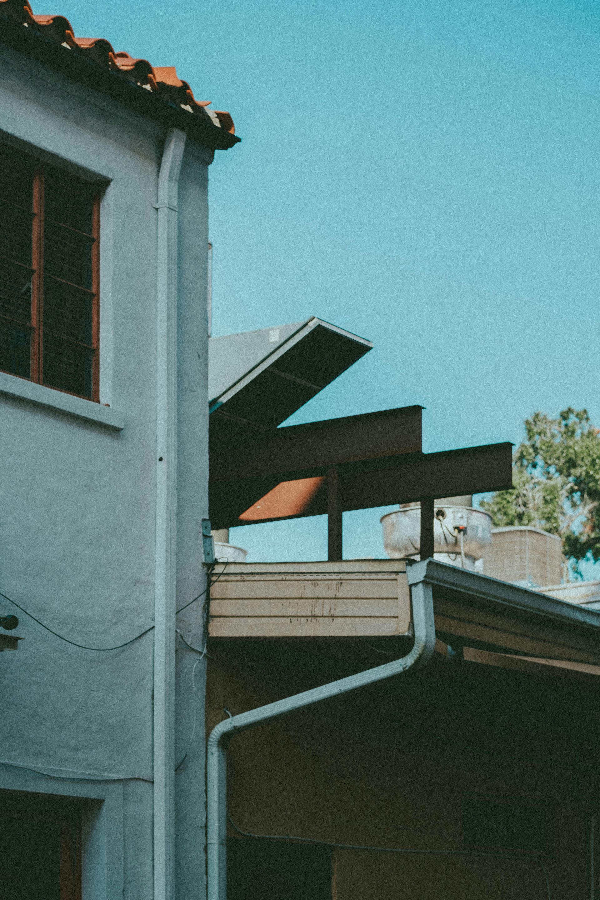 A side view of a white stucco building with a red-tiled roof and exposed steel beams extending over a porch area.
