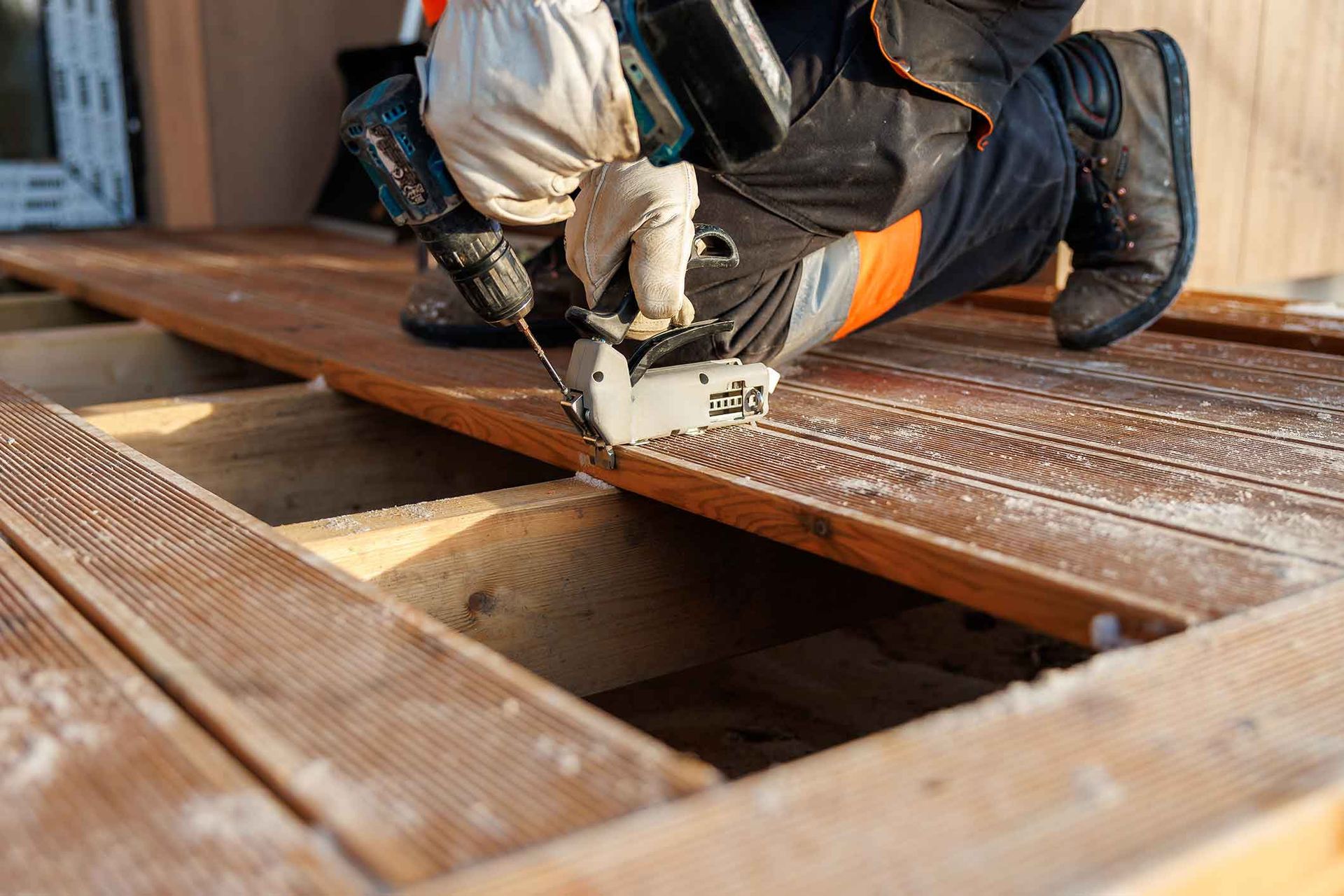 Person using a saw to cut a wooden plank on a deck, with sawdust visible.