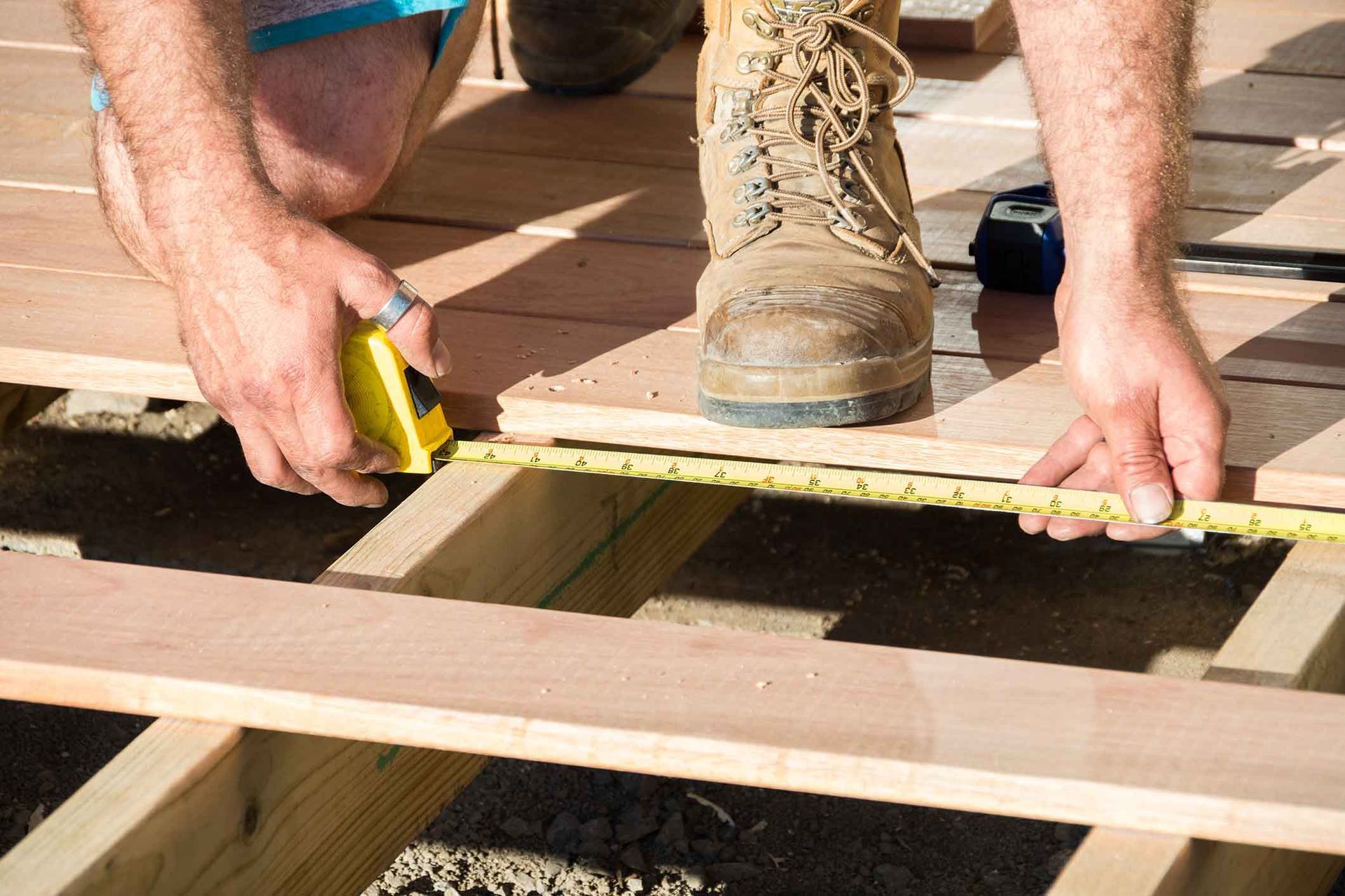 Person using a yellow tape measure to measure a wooden plank on a deck frame.